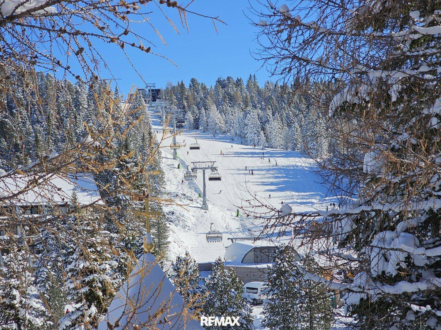 Blick auf eine belebte Skipiste mit Skiliften, umrahmt von verschneiten Bäumen.
