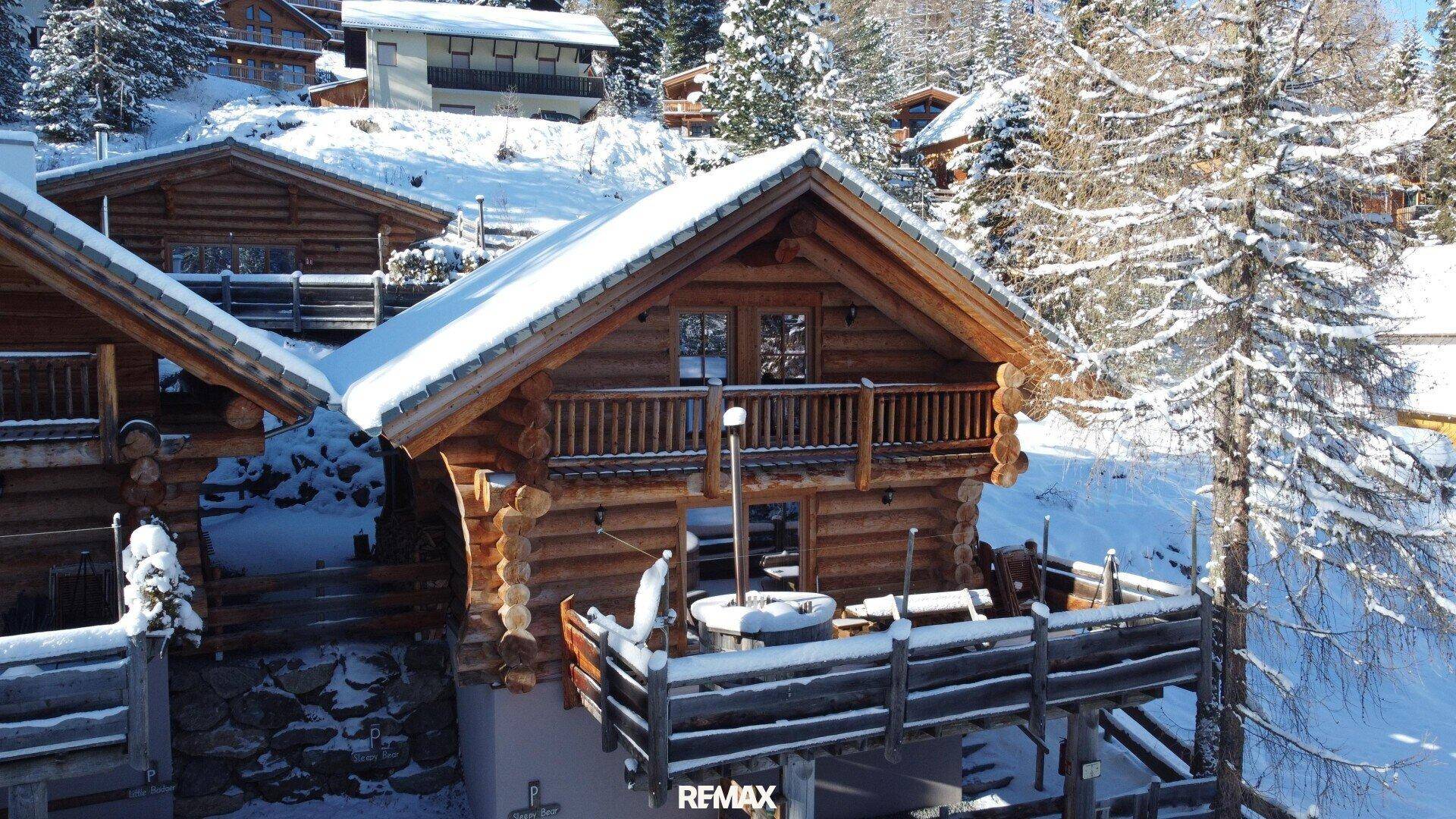 Charmantes Holzchalet mit Balkon und einem schneebedeckten Whirlpool auf der Terrasse.