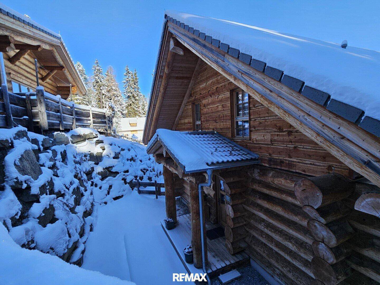Seitlicher Blick auf ein Holzchalet mit überdachtem Eingangsbereich und verschneitem Weg.