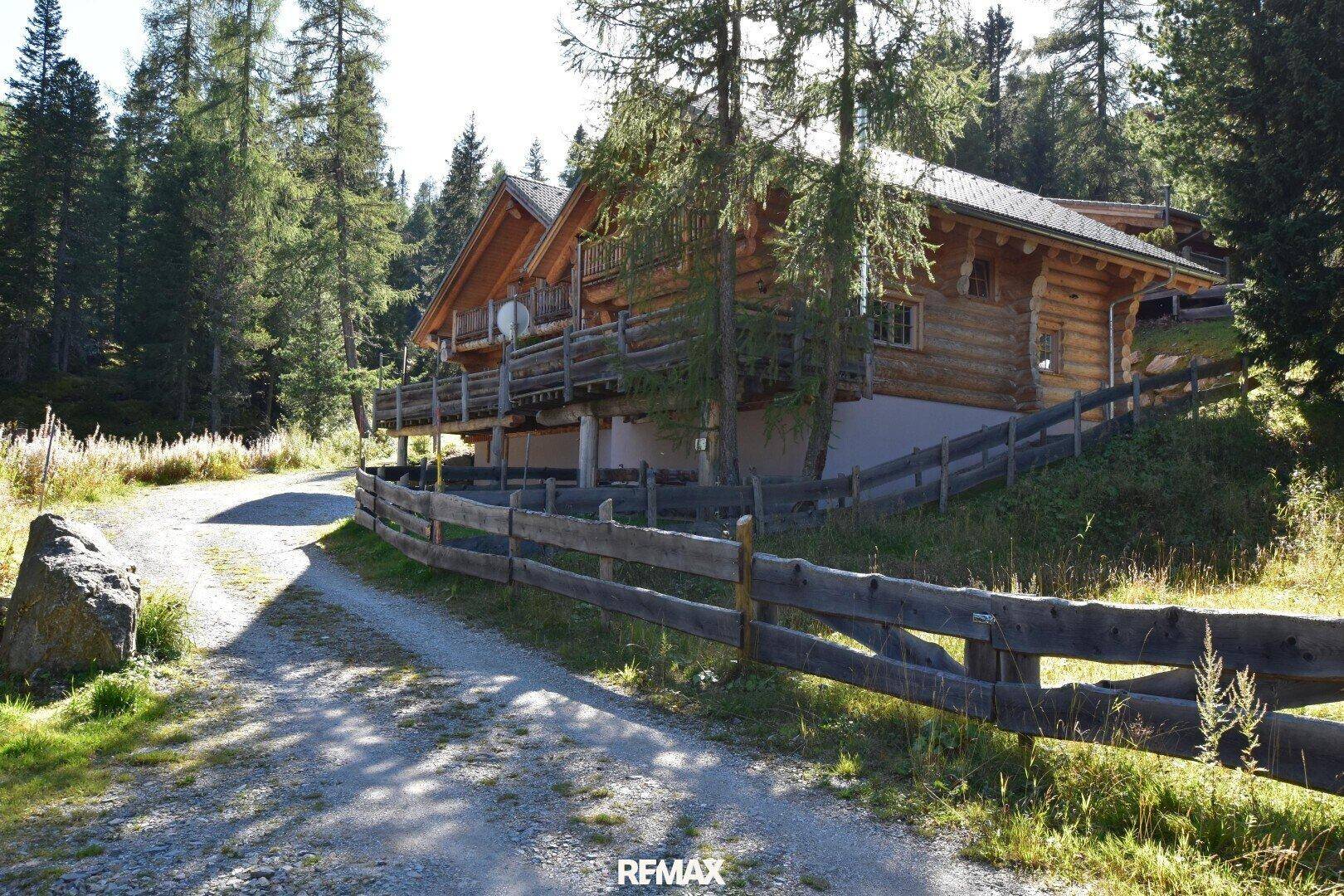 Rustikales Holzchalet in einer grünen, bewaldeten Berglandschaft an einem sonnigen Tag.