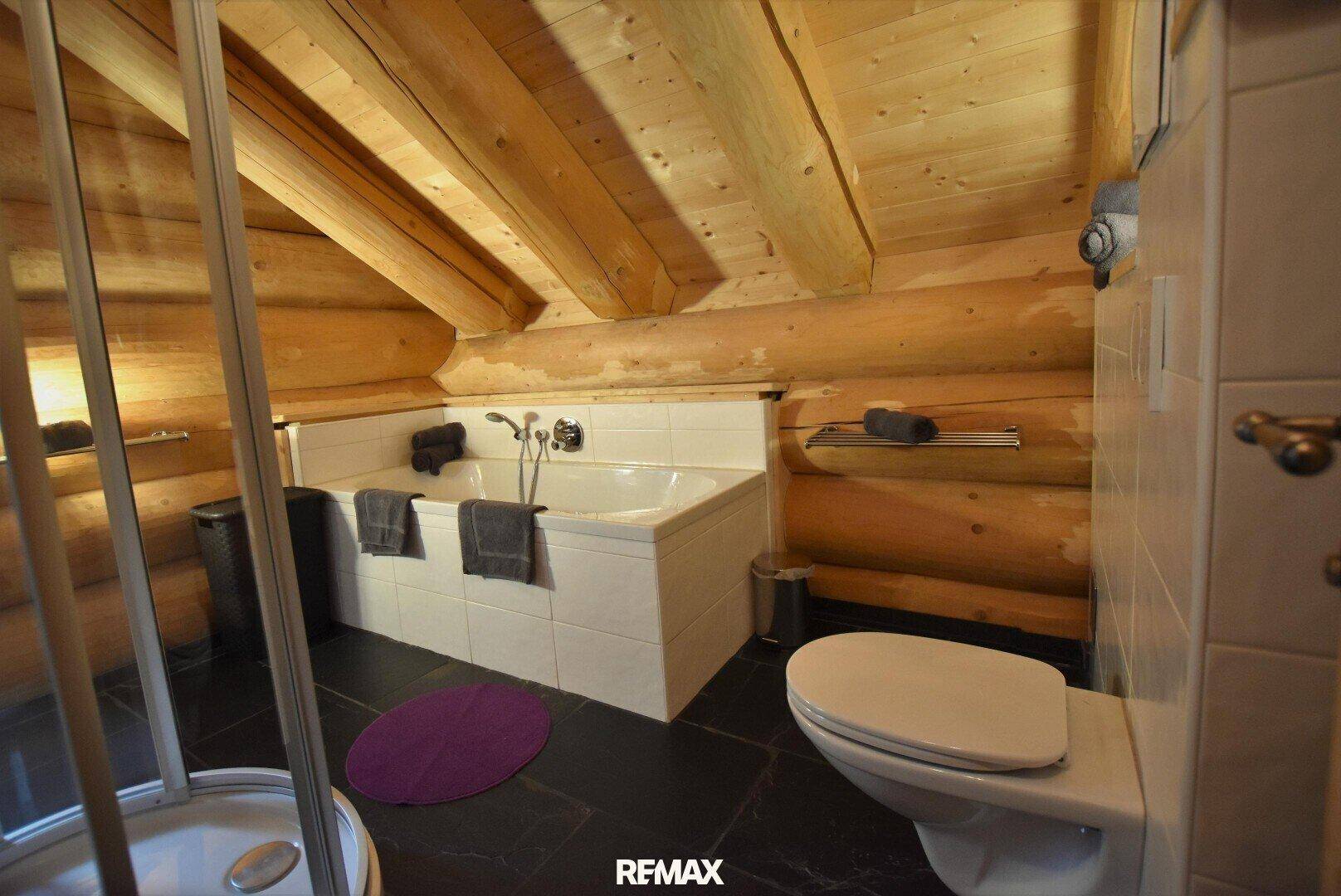 Badezimmer mit Badewanne, WC und Dachschräge, ausgestattet mit Holzwänden und Fliesenboden.