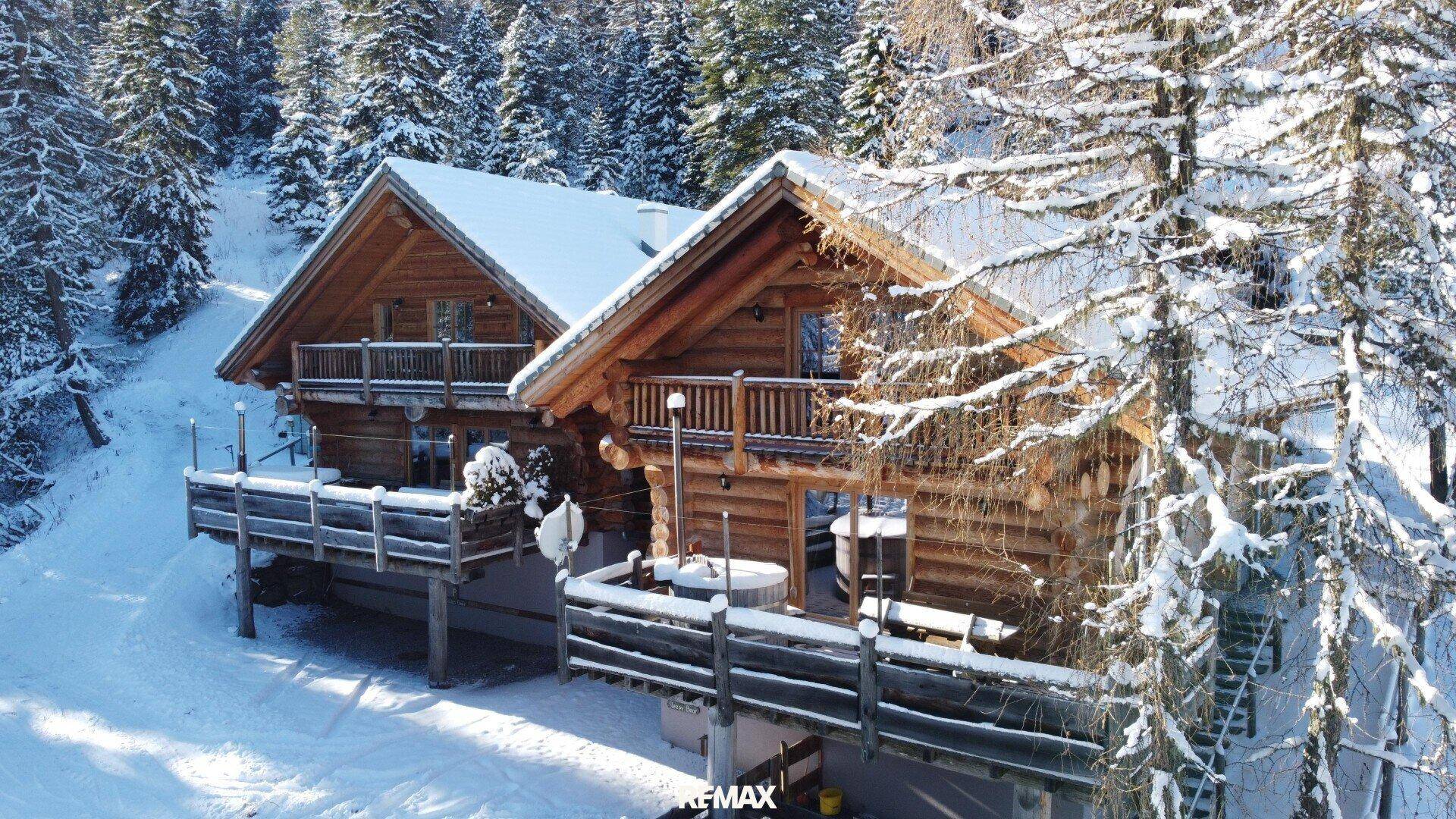 Blockhäuser im Winter, bedeckt mit Schnee, umgeben von verschneiten Bäumen und einer idyllischen Landschaft.