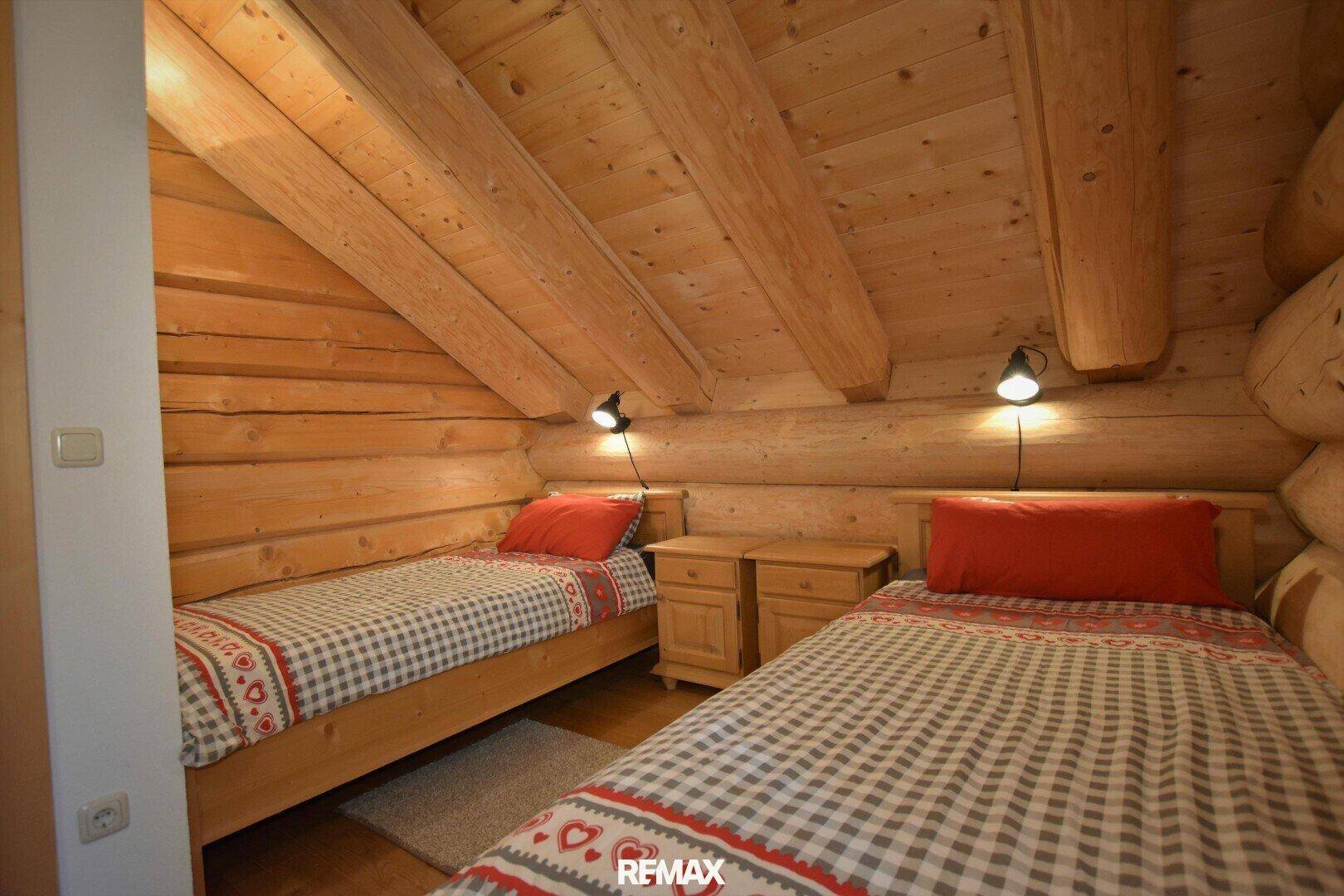 Gemütliches Schlafzimmer mit zwei Einzelbetten, Holzwänden und Dachschrägen im alpinen Stil.