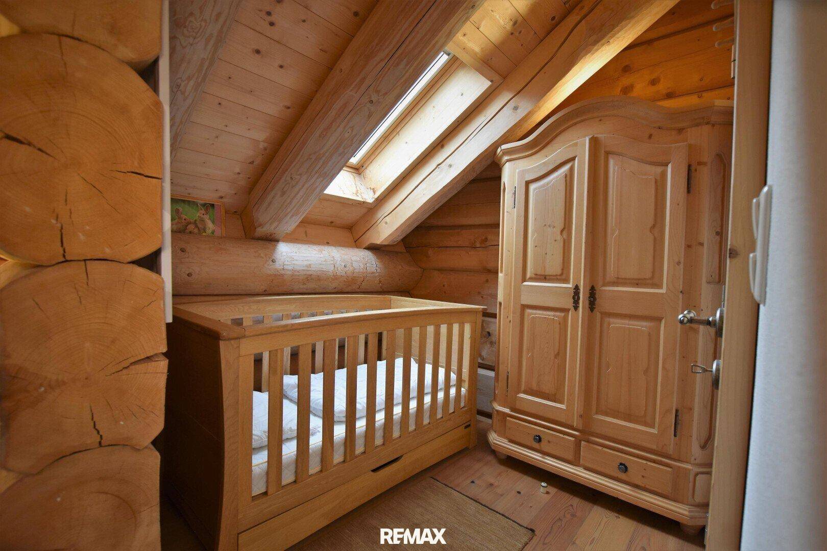 Kinderzimmer mit Babybett, Holzschrank und Dachfenster, das viel natürliches Licht spendet.