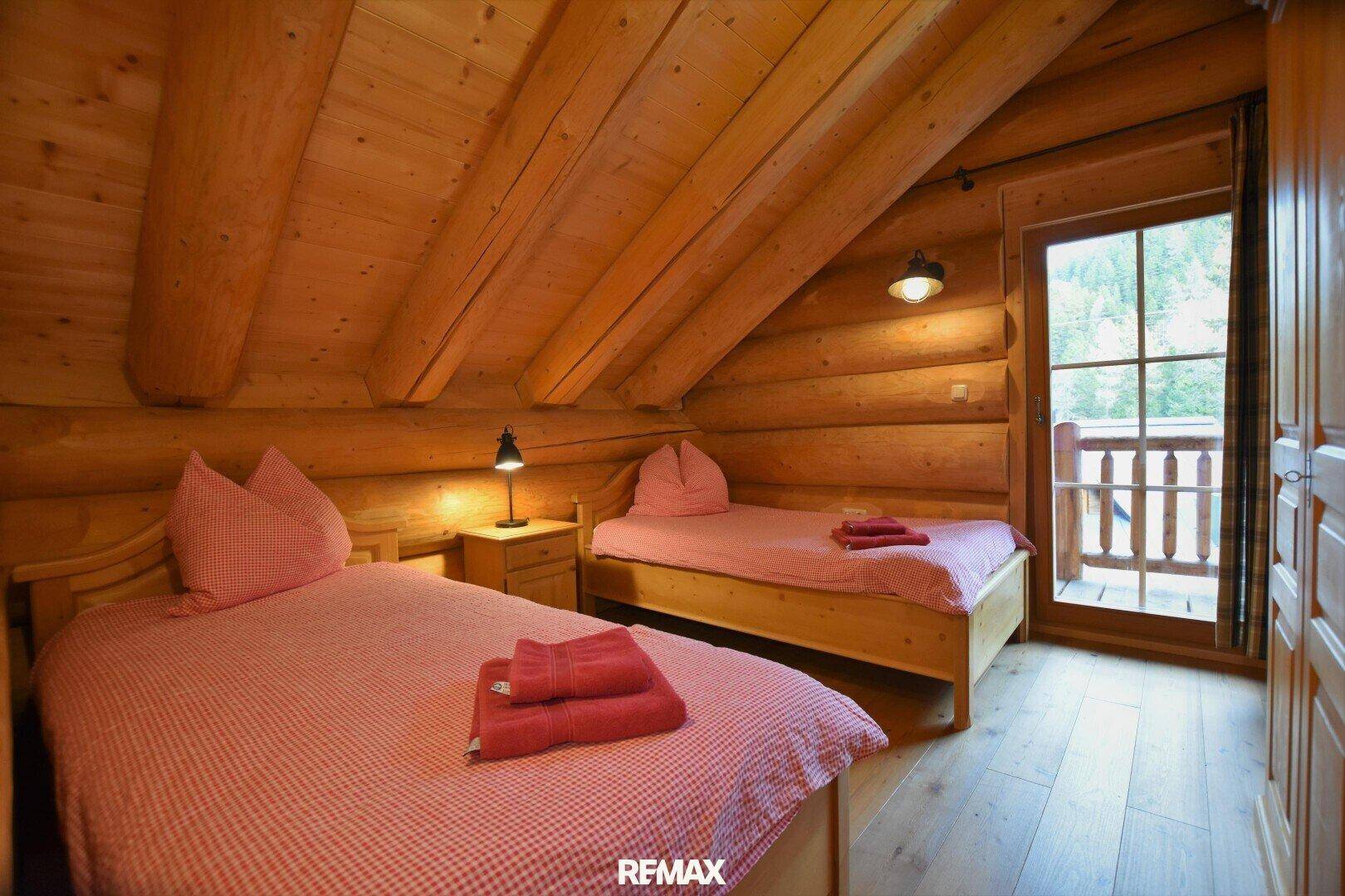 Schlafzimmer mit zwei Einzelbetten, Holzwänden und Zugang zu einem kleinen Balkon.