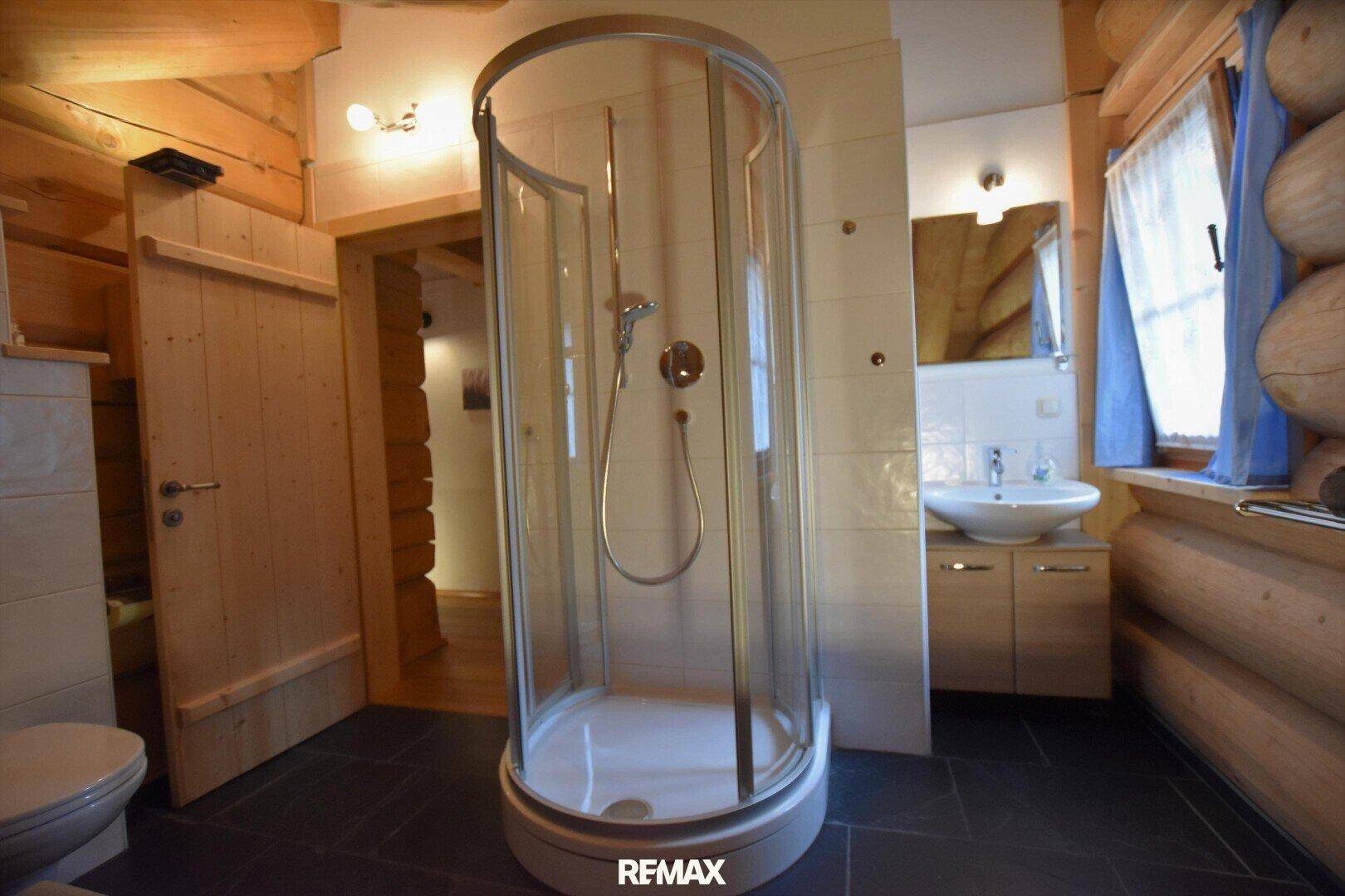 Badezimmer mit Duschkabine, Waschbecken und WC, umgeben von Holzwänden und Fliesenboden.
