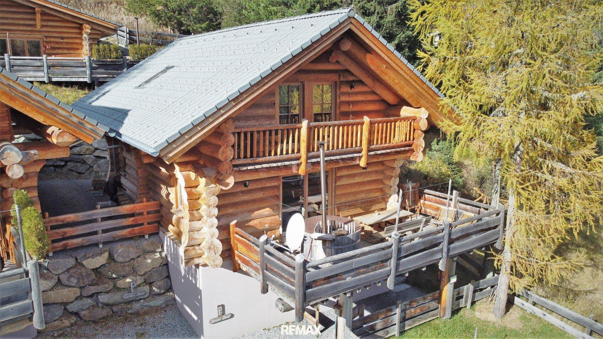 Blockhausfassade mit rustikalem Balkon und einer Holzterrasse, umgeben von alpiner Natur.