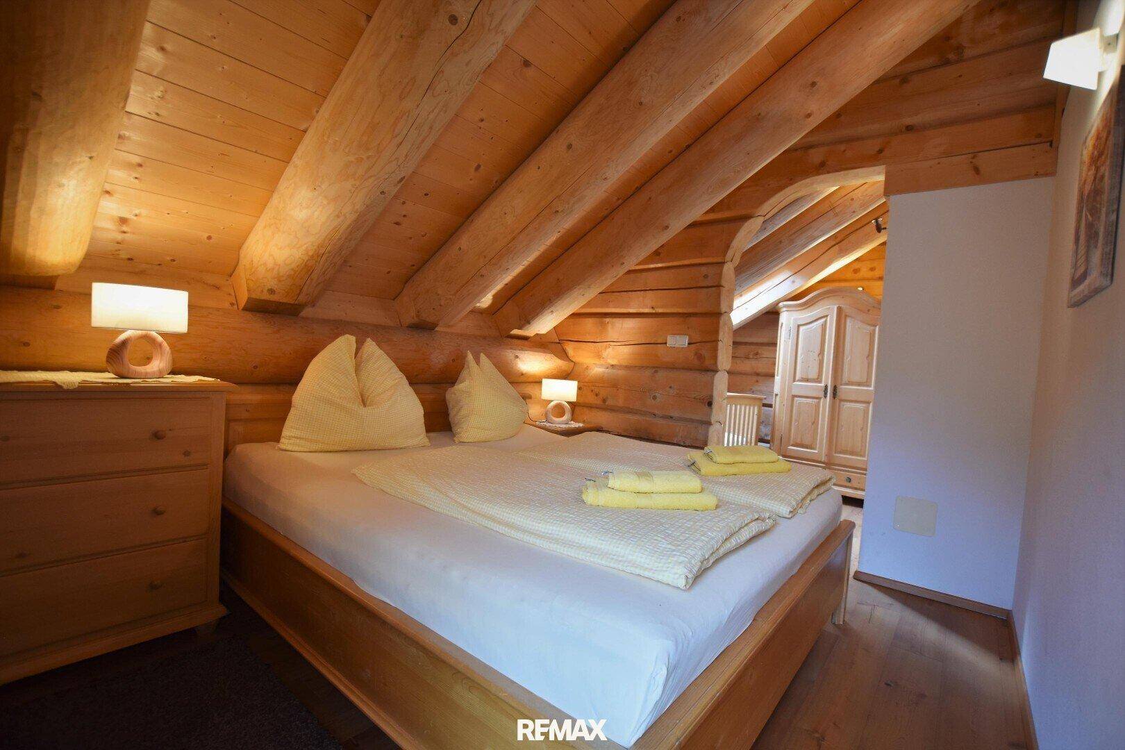 Schlafzimmer mit Doppelbett, rustikalem Holzschrank und Holzwänden unter der Dachschräge.
