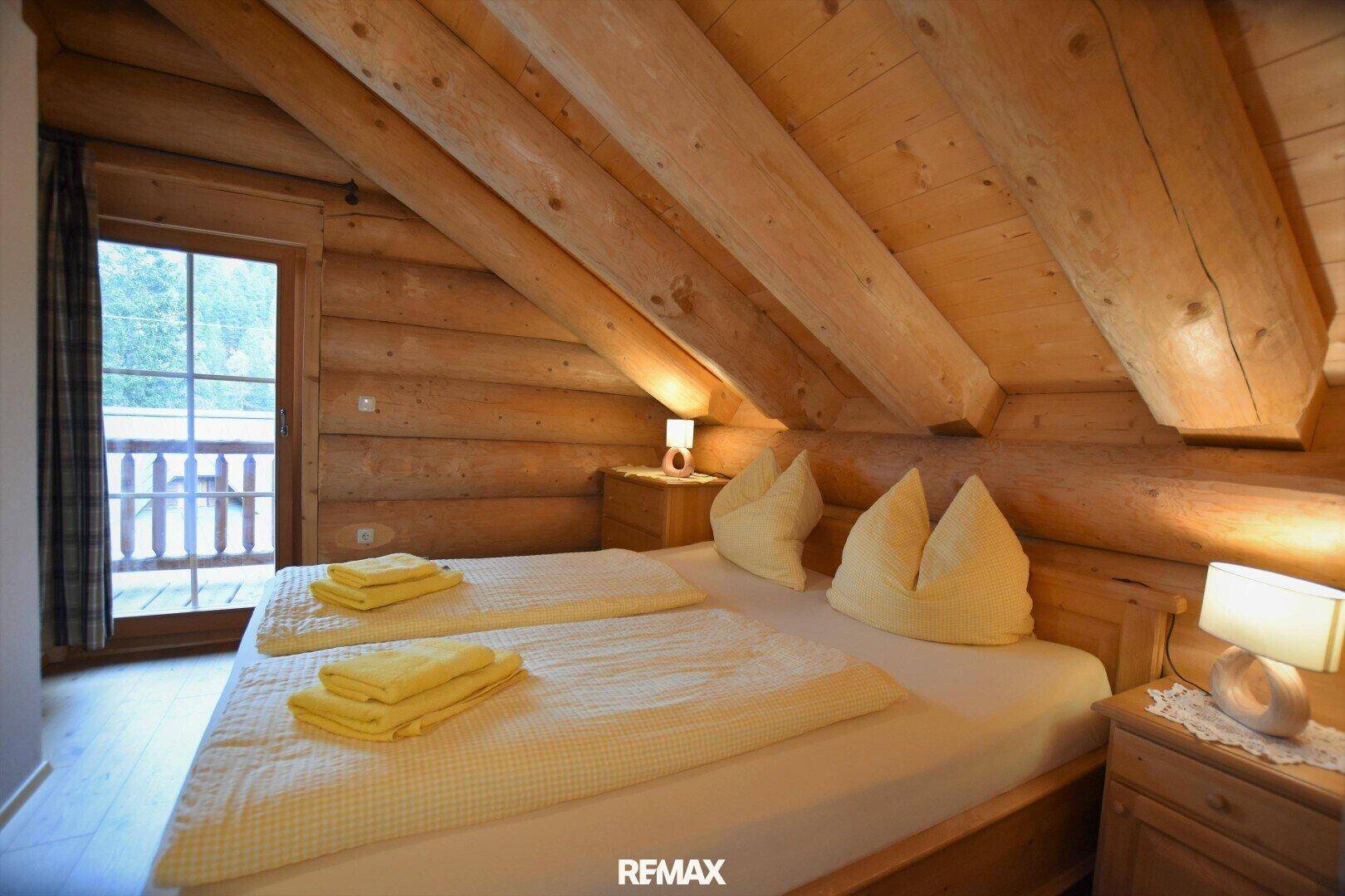 Gemütliches Schlafzimmer mit Doppelbett, Holzbalken und Balkonzugang im Dachgeschoss.