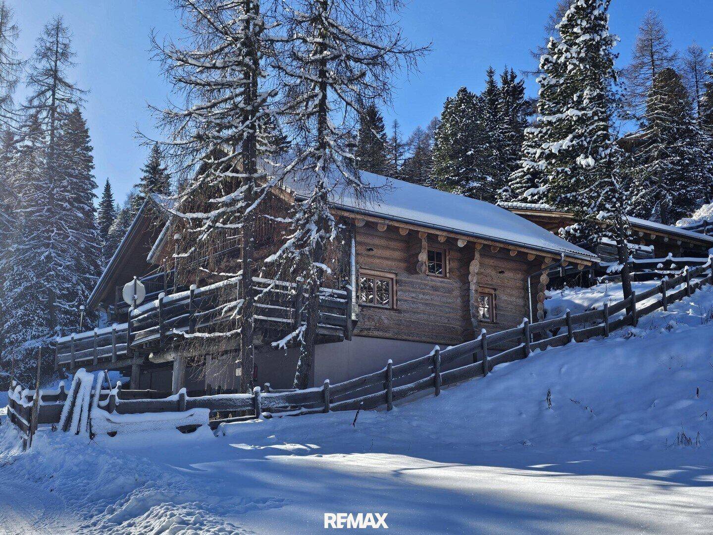 Gemütliches Holzchalet in verschneiter Berglandschaft unter strahlend blauem Himmel.