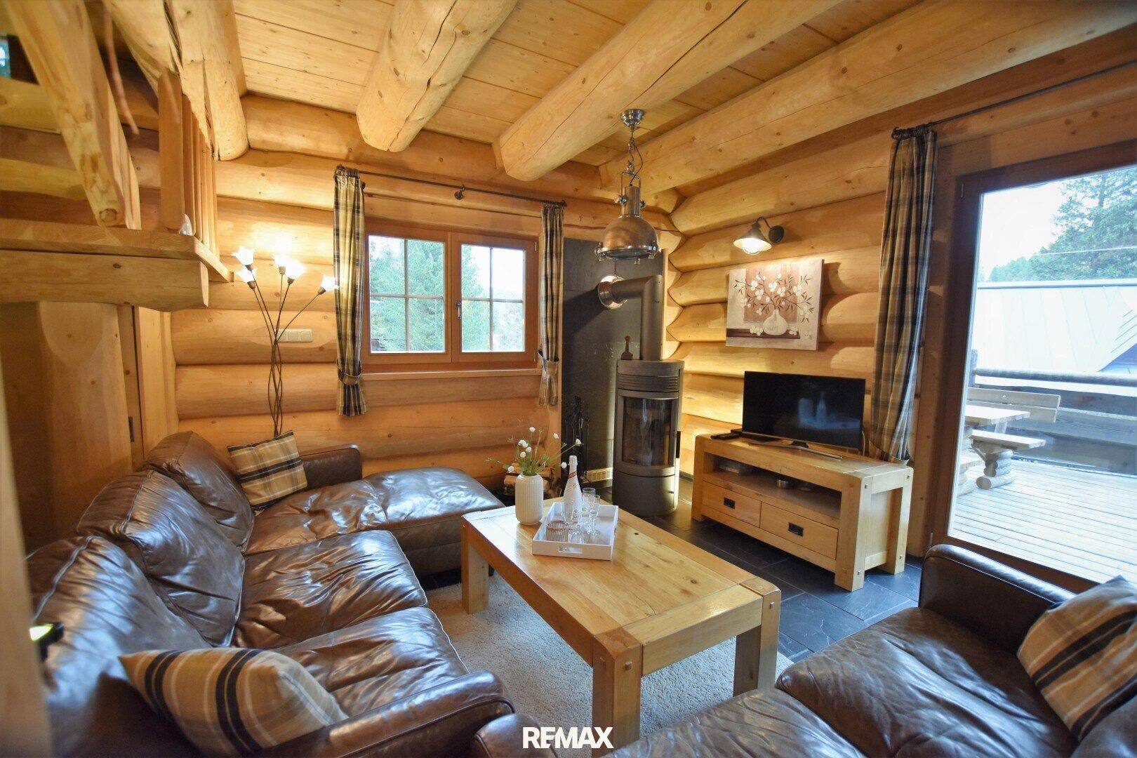 Gemütliches Wohnzimmer im Blockhausstil mit Ledersofas, Kaminofen und Zugang zur Terrasse.