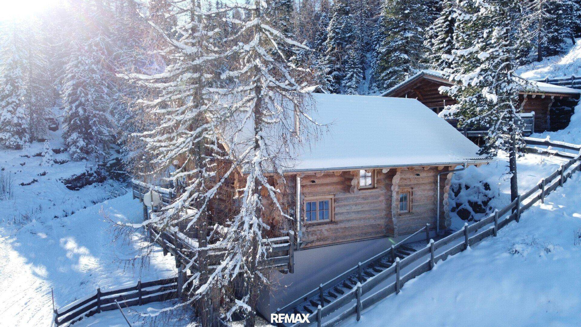 Einzelnes Blockhaus im Winter, umgeben von tiefem Schnee und verschneiten Nadelbäumen.