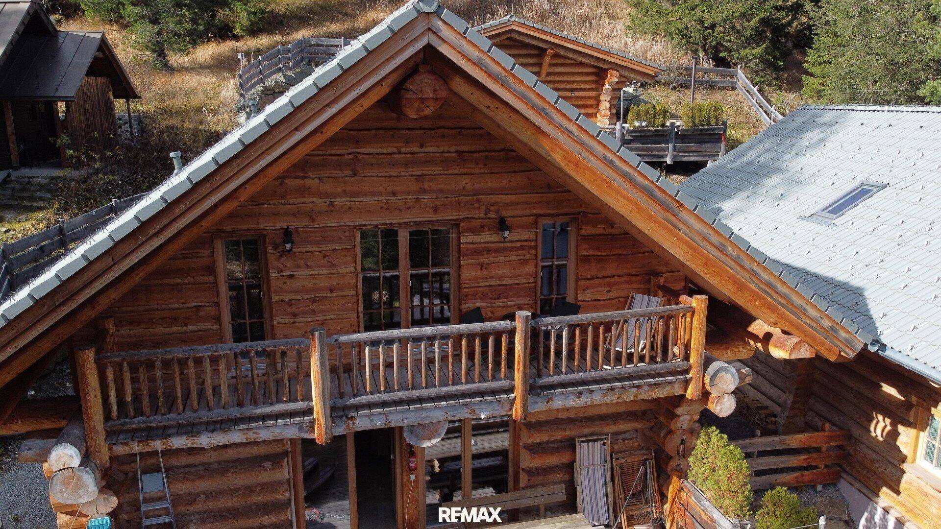 Ansicht eines Holzchalets mit Balkon und traditioneller Holzfassade in alpiner Umgebung.