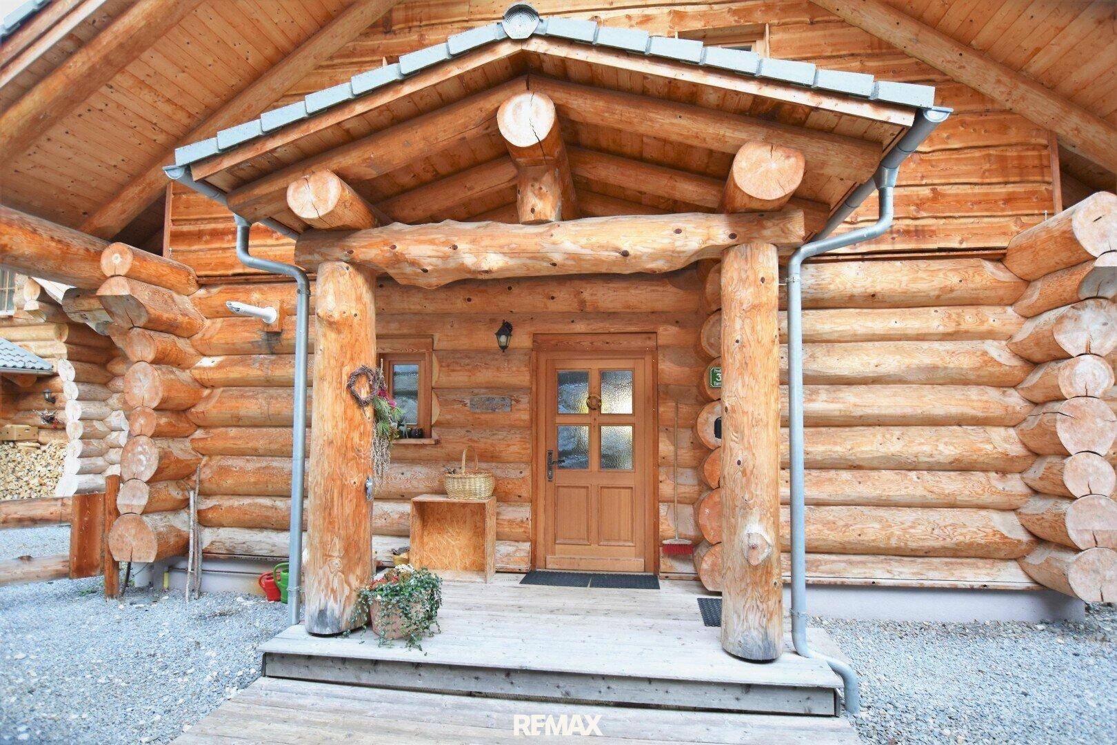 Haupteingang eines rustikalen Holzchalets mit überdachtem Vordach und Holztür.