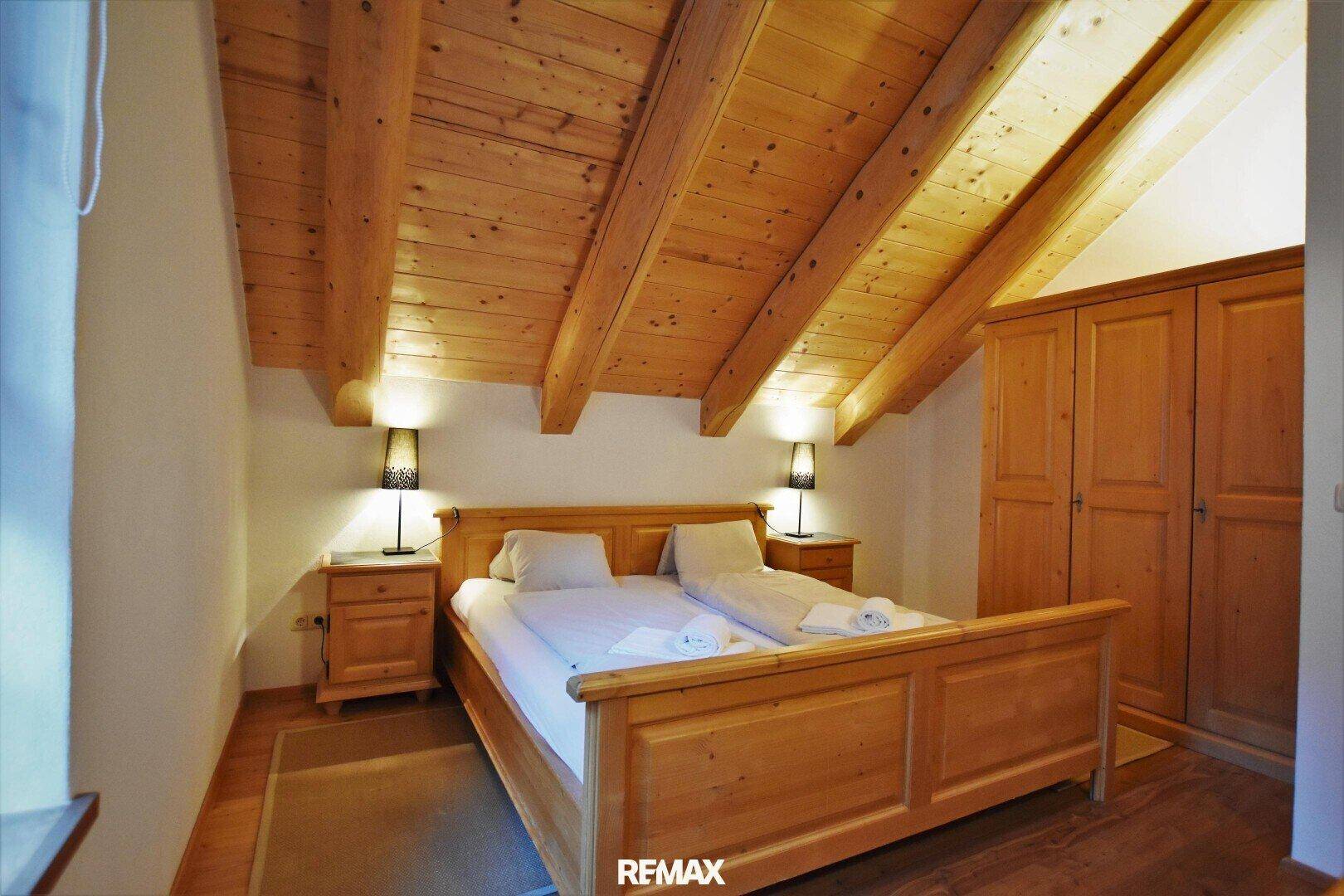 Gemütliches Schlafzimmer im Dachgeschoss mit Doppelbett, Holzschrank und Holzbalkendecke.