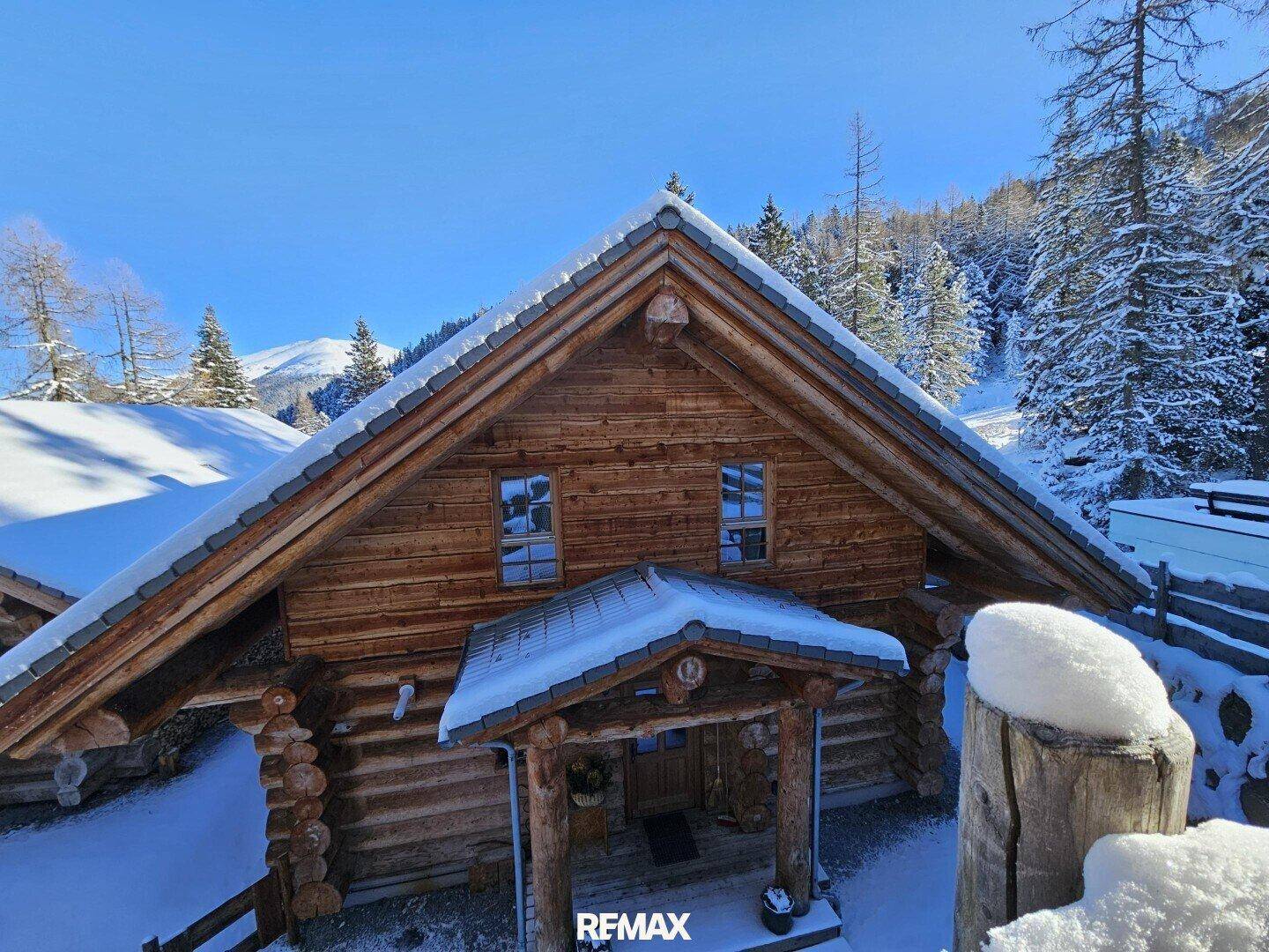 Vorderansicht eines Holzchalets im Winter mit schneebedecktem Dach und Eingangsbereich.