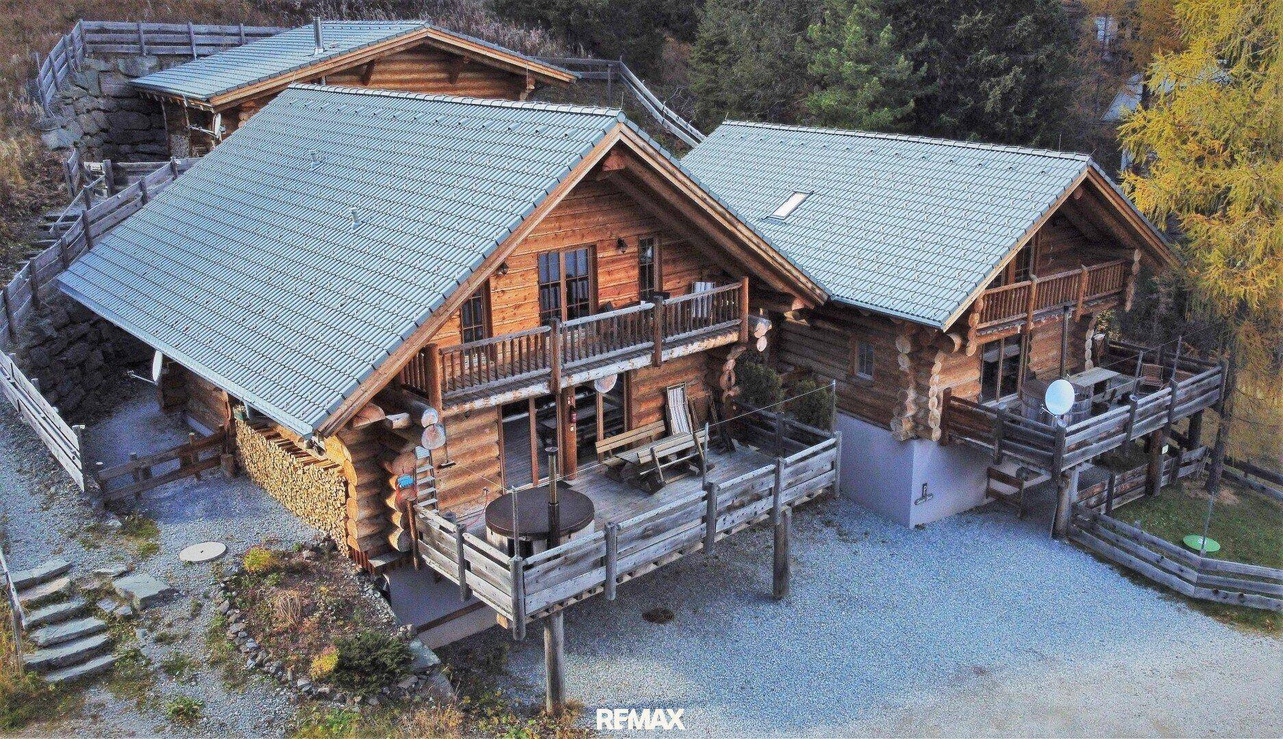 Weitläufige Ansicht eines Holzchalets mit mehreren Terrassen und Balkonen in bergiger Umgebung.