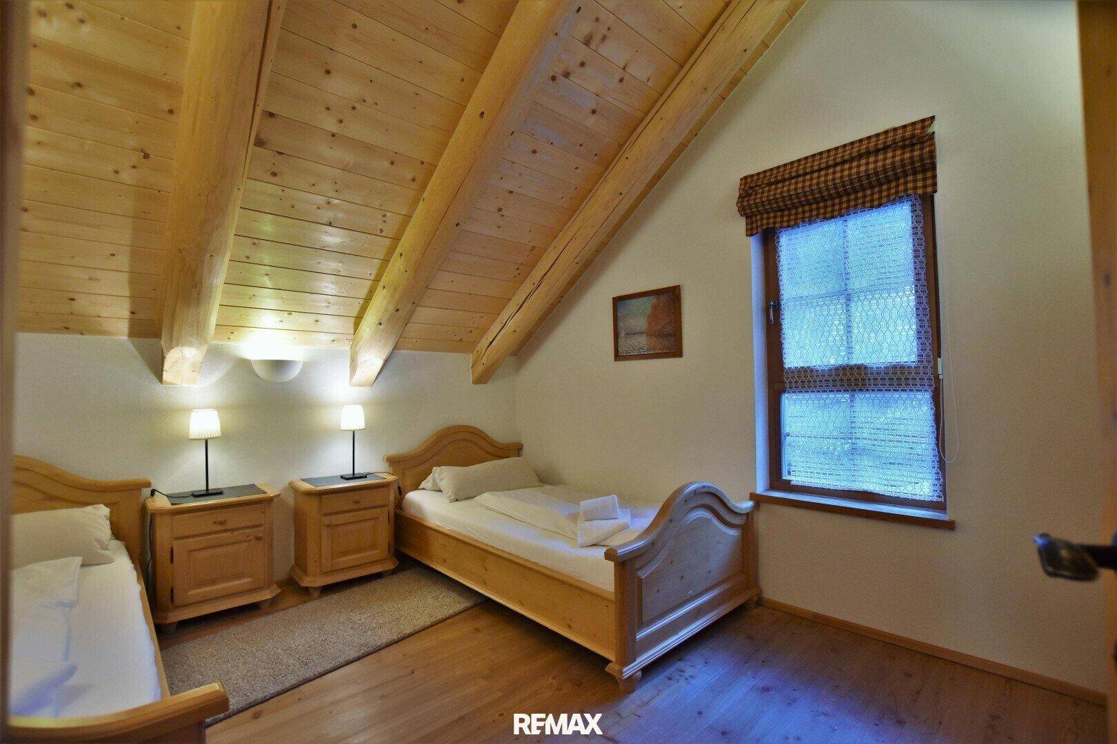 Schlafzimmer im Dachgeschoss mit Holzbett, Nachttischen und sichtbaren Holzbalken.