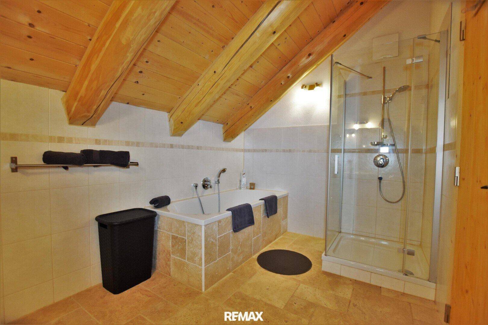 Badezimmer im Dachgeschoss mit Badewanne, Duschkabine und sichtbaren Holzbalken.