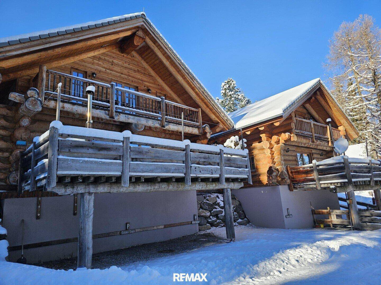 Winterliche Ansicht der Holzchalets mit schneebedeckten Terrassen und strahlendem Sonnenschein.