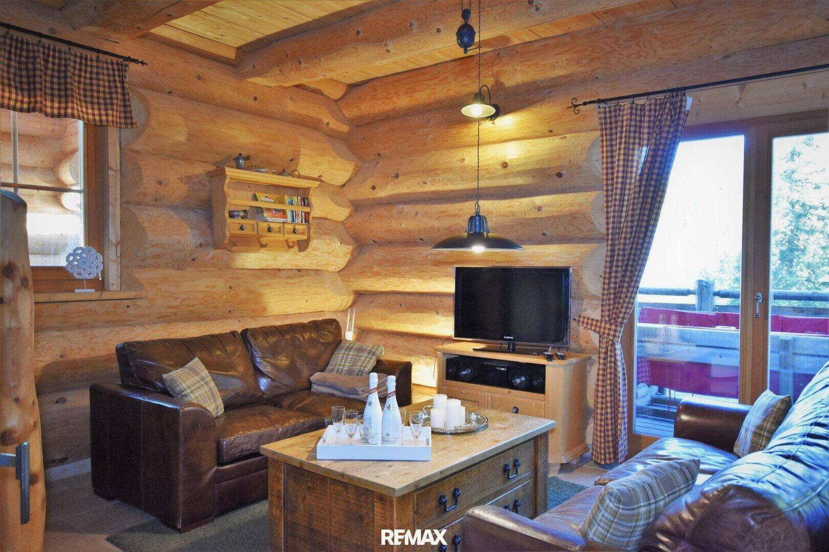 Rustikales Wohnzimmer mit Holzwänden, Ledersofas und Zugang zu einem Außenbereich.