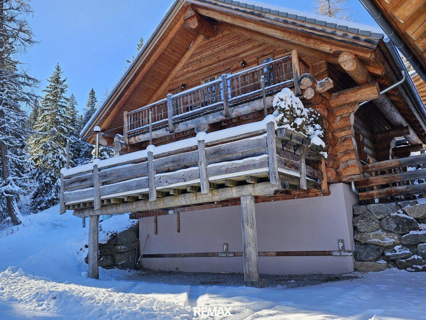 Schneebedeckte Holzterrasse eines Chalets mit Blick auf die winterliche Berglandschaft.