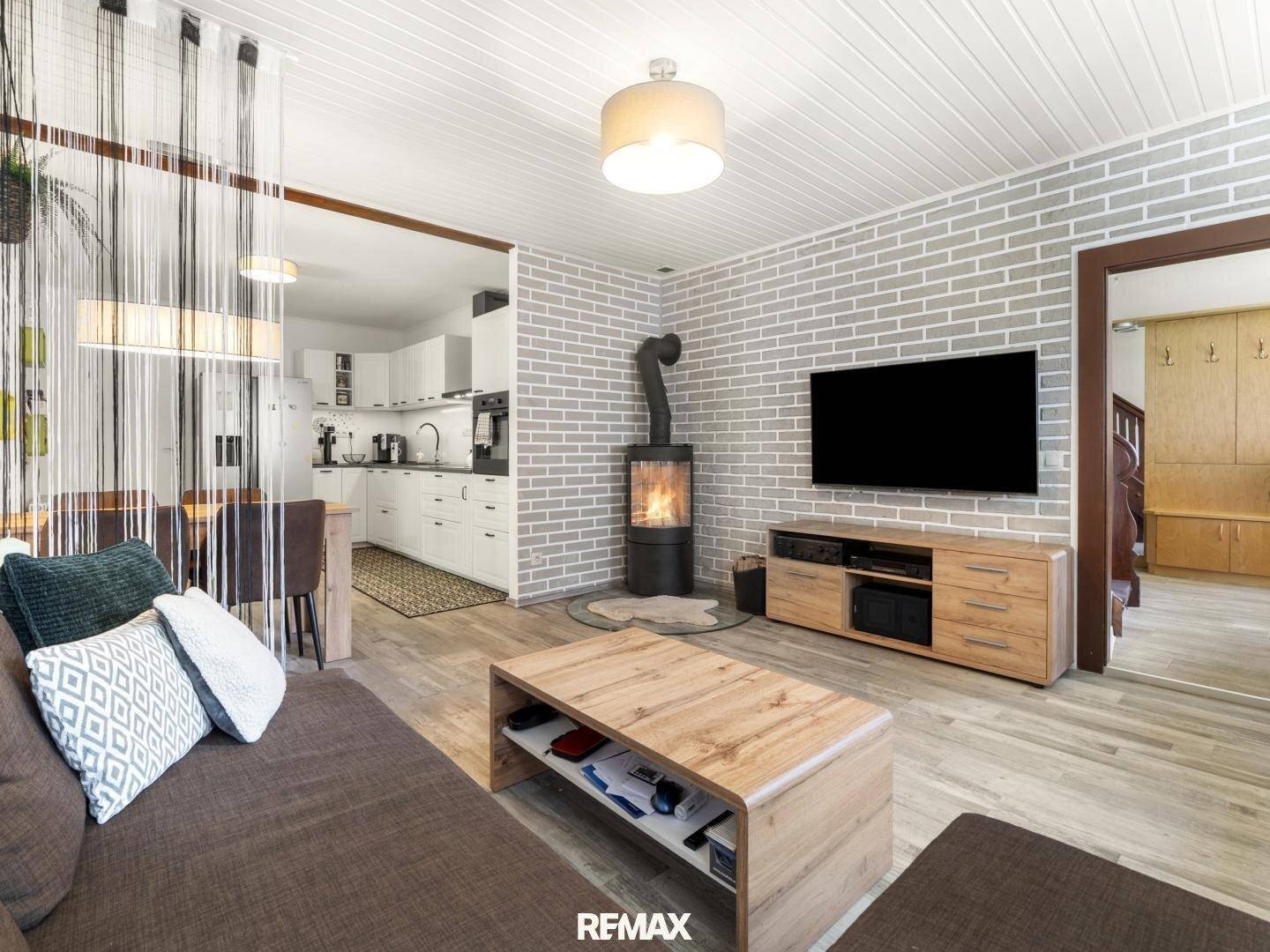 Offener Wohnbereich mit Kaminofen, Fernseher und Blick in die angrenzende Küche, mit Holzboden.