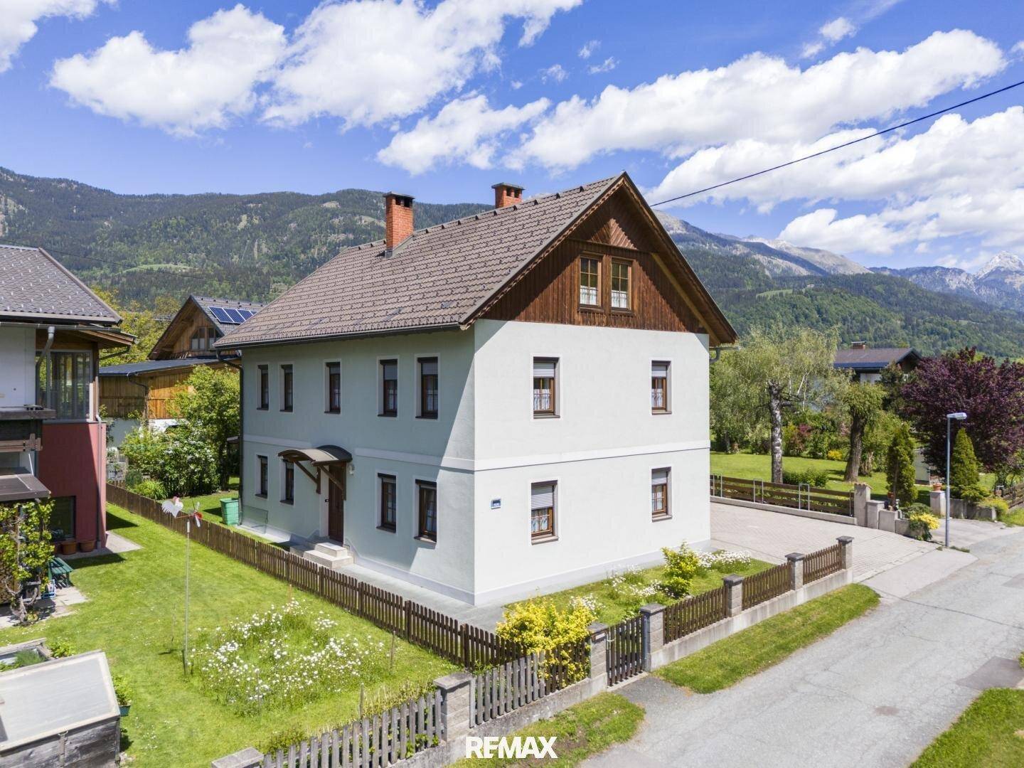 Ansicht des Hauses von der Straßenseite mit gepflegtem Vorgarten und Holzzaun in bergiger Landschaft.