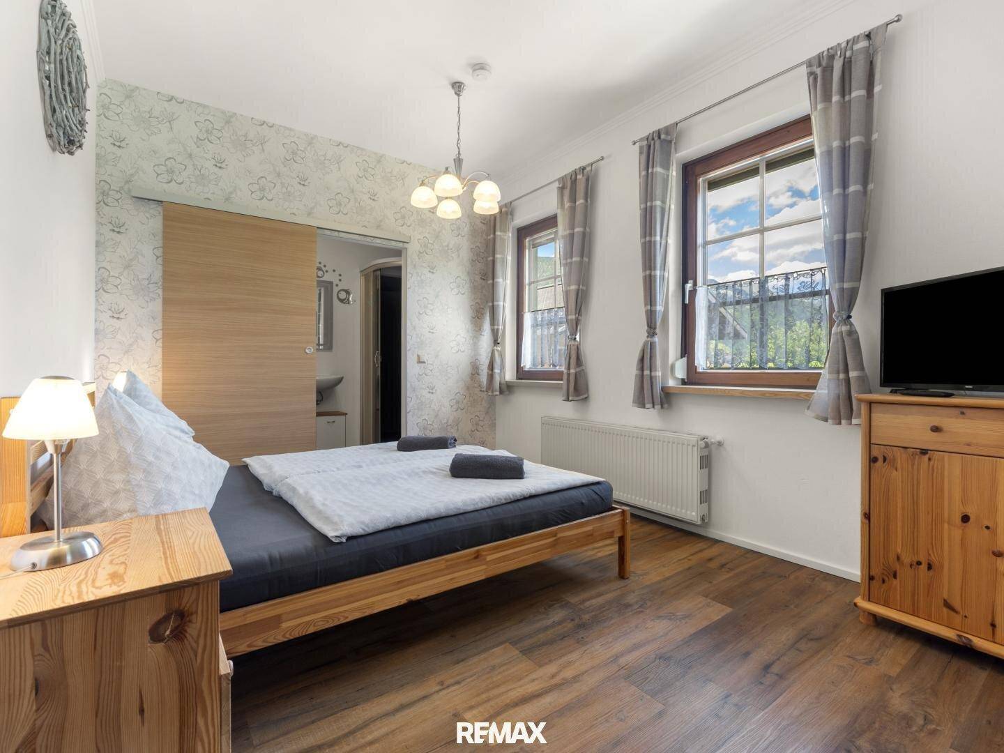 Schlafzimmer mit Holzboden, floraler Tapete und Zugang zu einem angrenzenden Badezimmer.