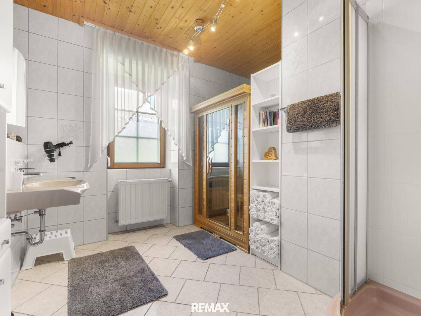Badezimmer mit Fliesenboden, Waschbecken und einer integrierten Sauna für Wellnessmomente.