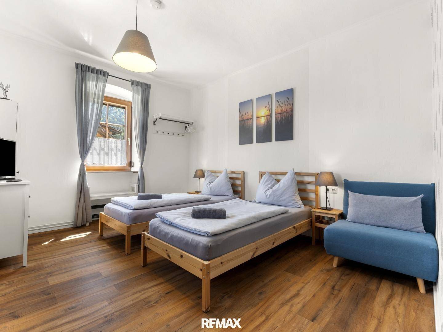 Helles Schlafzimmer mit zwei Einzelbetten, Holzboden und einem kleinen Sofa.