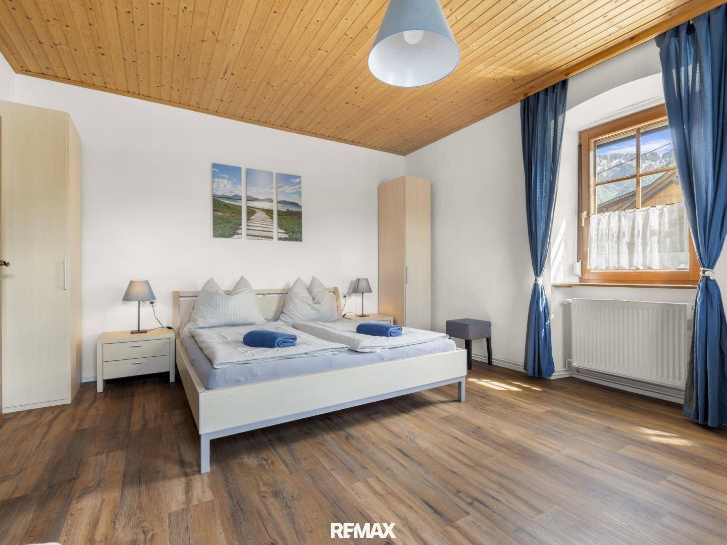 Gemütliches Schlafzimmer mit Holzbalkendecke, Doppelbett und Blick auf die Berge durch das Fenster.