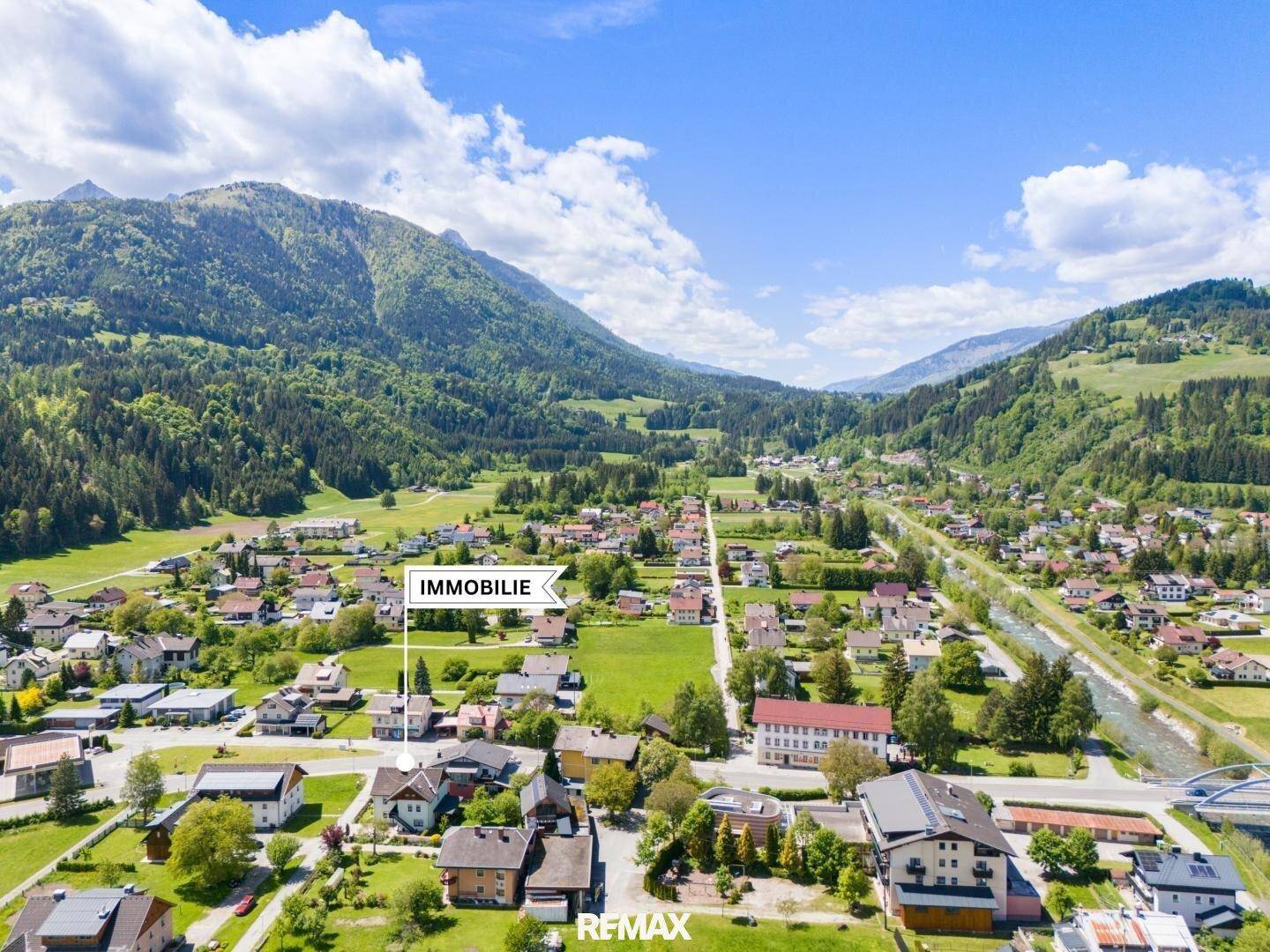 Luftaufnahme der Immobilie in einer malerischen Berglandschaft mit umliegenden Häusern und viel Grün.