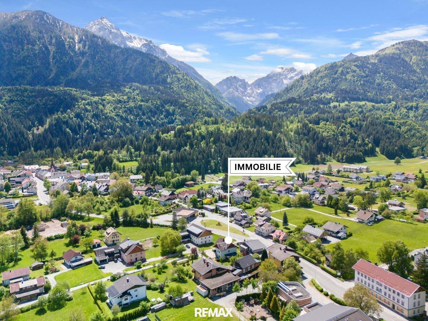 Panoramablick aus der Vogelperspektive auf die Immobilie, eingebettet in eine idyllische Bergregion mit weiten Grünflächen.