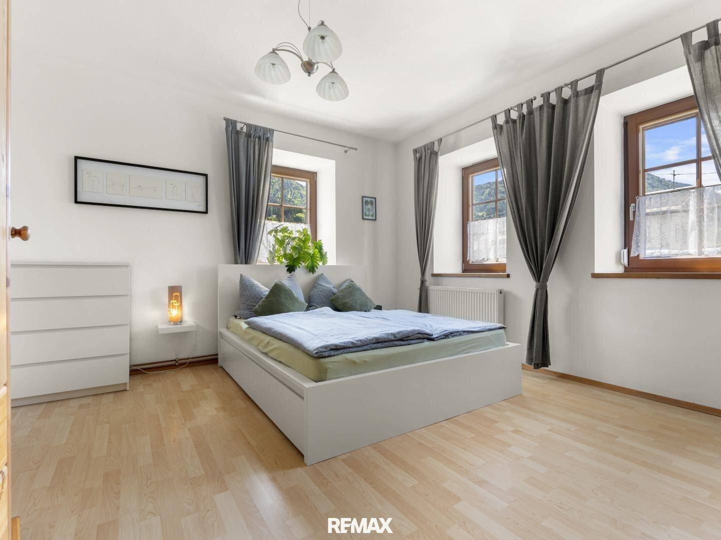 Helles Schlafzimmer mit Doppelbett, Holzfenstern und Laminatboden, bietet eine ruhige Atmosphäre.