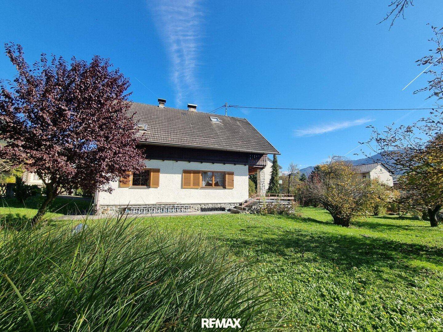 Rückansicht des Hauses mit weitläufigem Garten und Bäumen im Sonnenlicht.