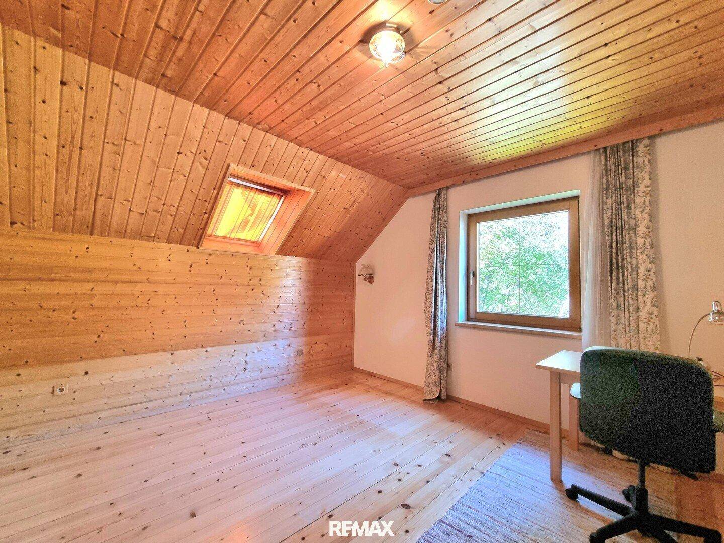 Helles Schlafzimmer im Dachgeschoss mit Holzverkleidung, Dachfenster und Schreibtisch.