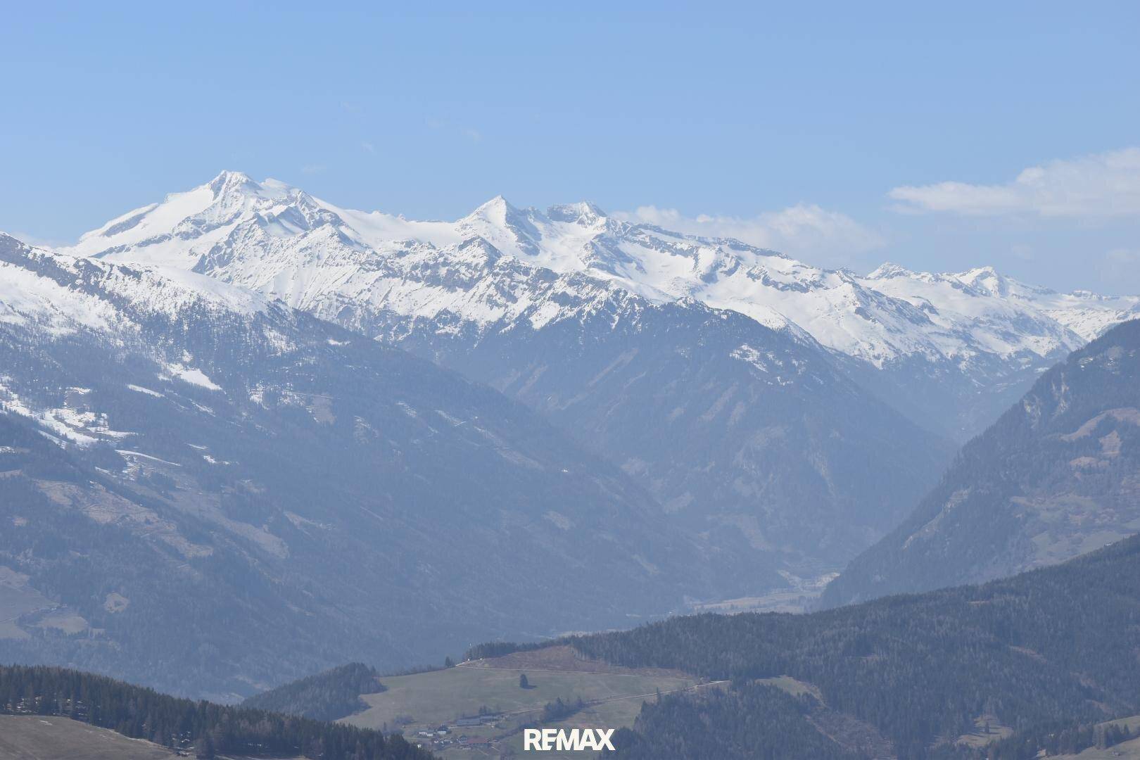 Majestätischer Blick auf schneebedeckte Alpengipfel und weite Täler unter einem klaren blauen Himmel.
