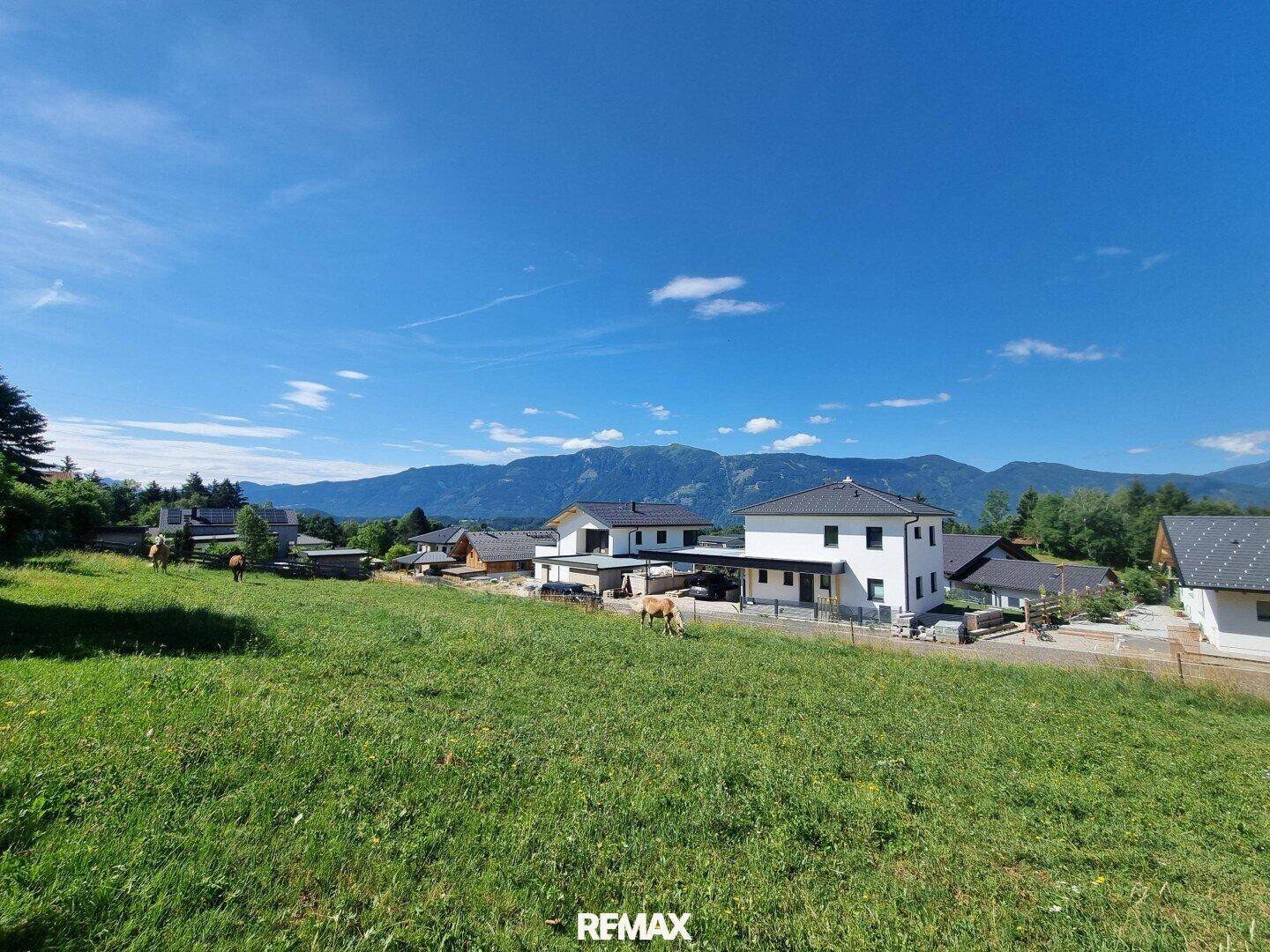Idyllische Landschaft mit modernen Wohnhäusern und majestätischem Bergblick unter blauem Himmel.