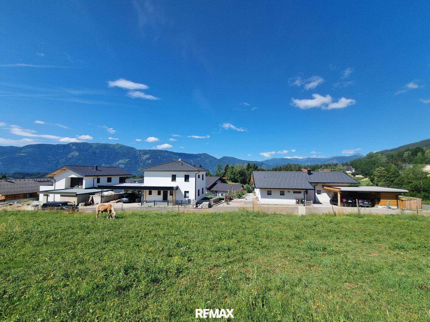 Panoramablick auf moderne Häuser und grüne Wiesen vor einer beeindruckenden Bergkulisse.
