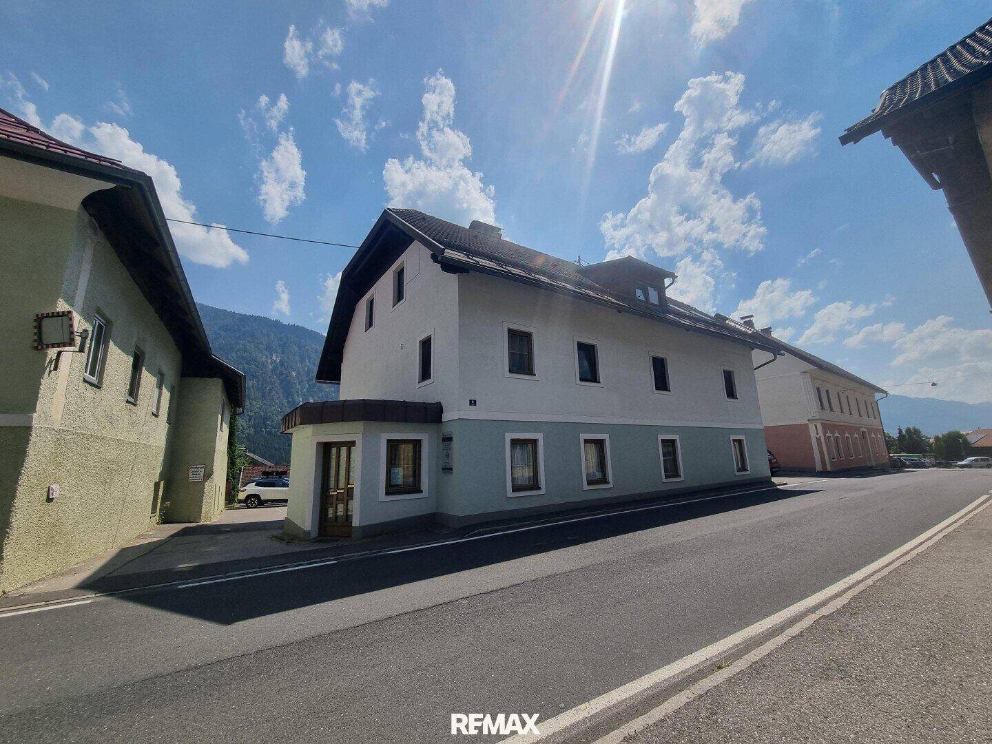 Traditionelles Gebäude an einer Straße mit Bergblick unter blauem Himmel.
