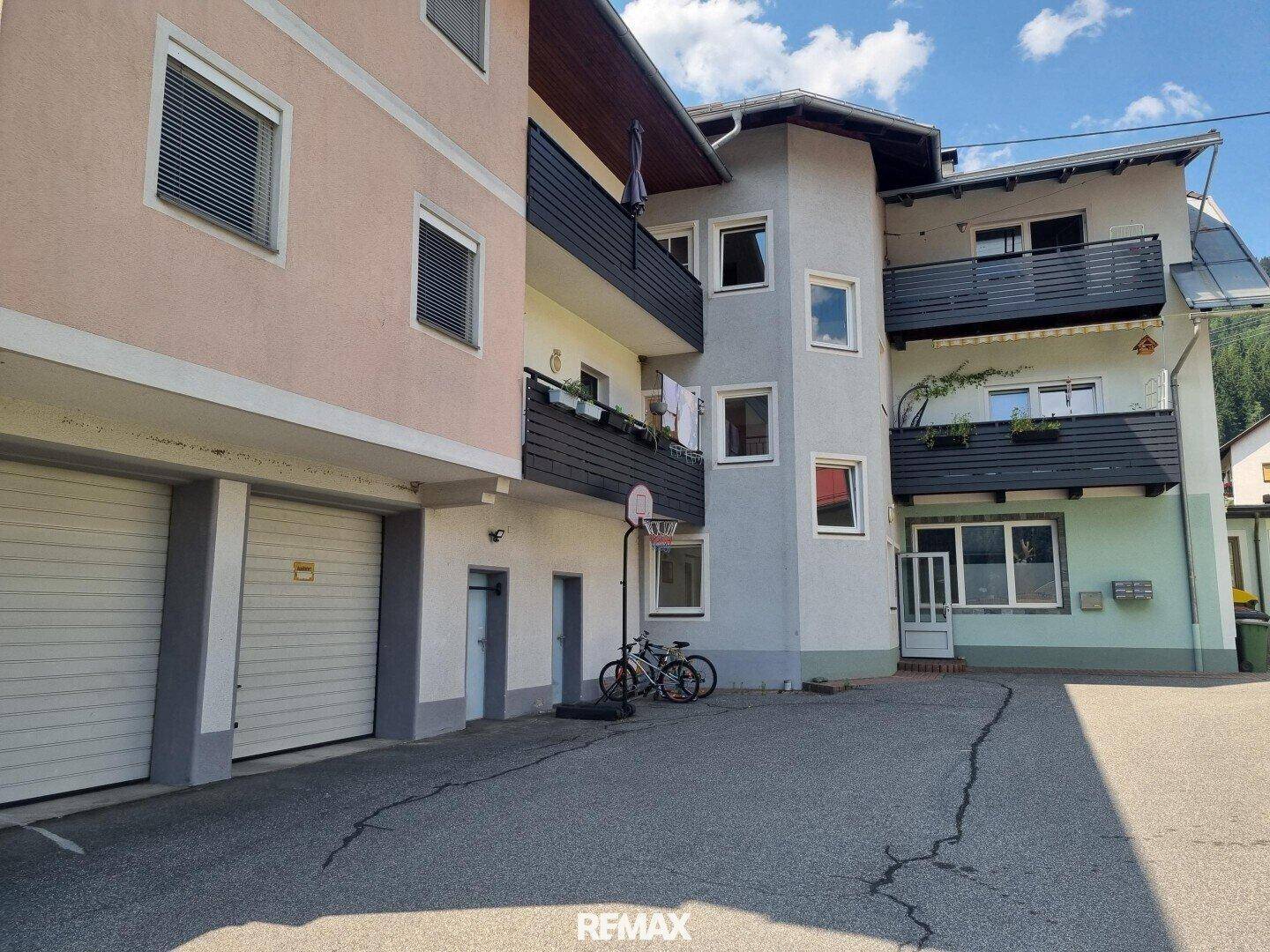 Mehrstöckiges Gebäude mit Balkonen und Garagen im Erdgeschoss, an einem sonnigen Tag.