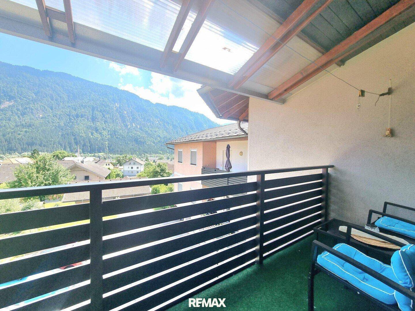 Überdachter Balkon mit Sitzgelegenheiten und Kunstrasen, bietet einen schönen Blick auf die Berge.