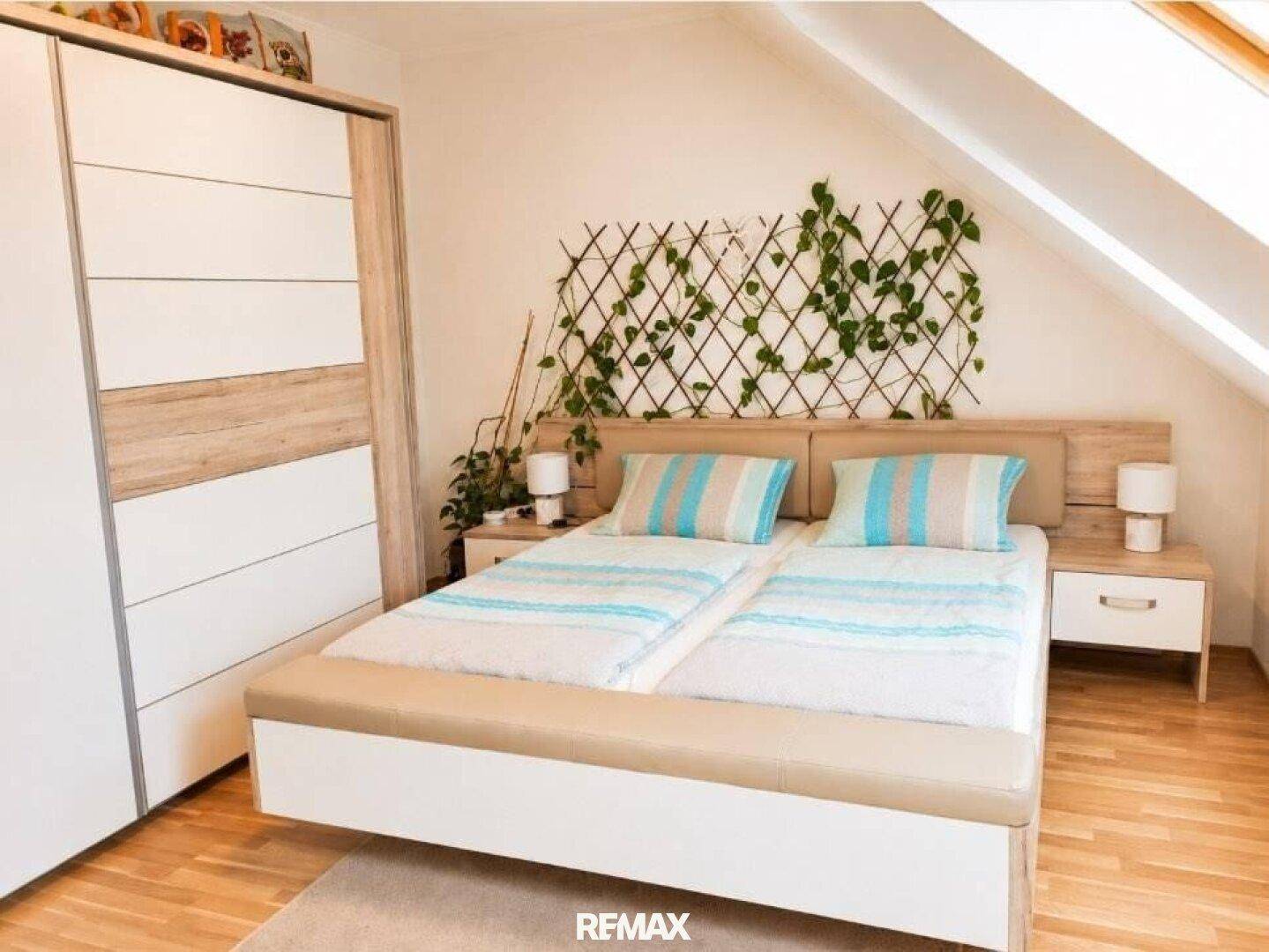 Gemütliches Schlafzimmer im Dachgeschoss mit Doppelbett, Kleiderschrank und dekorativer Wandbegrünung.