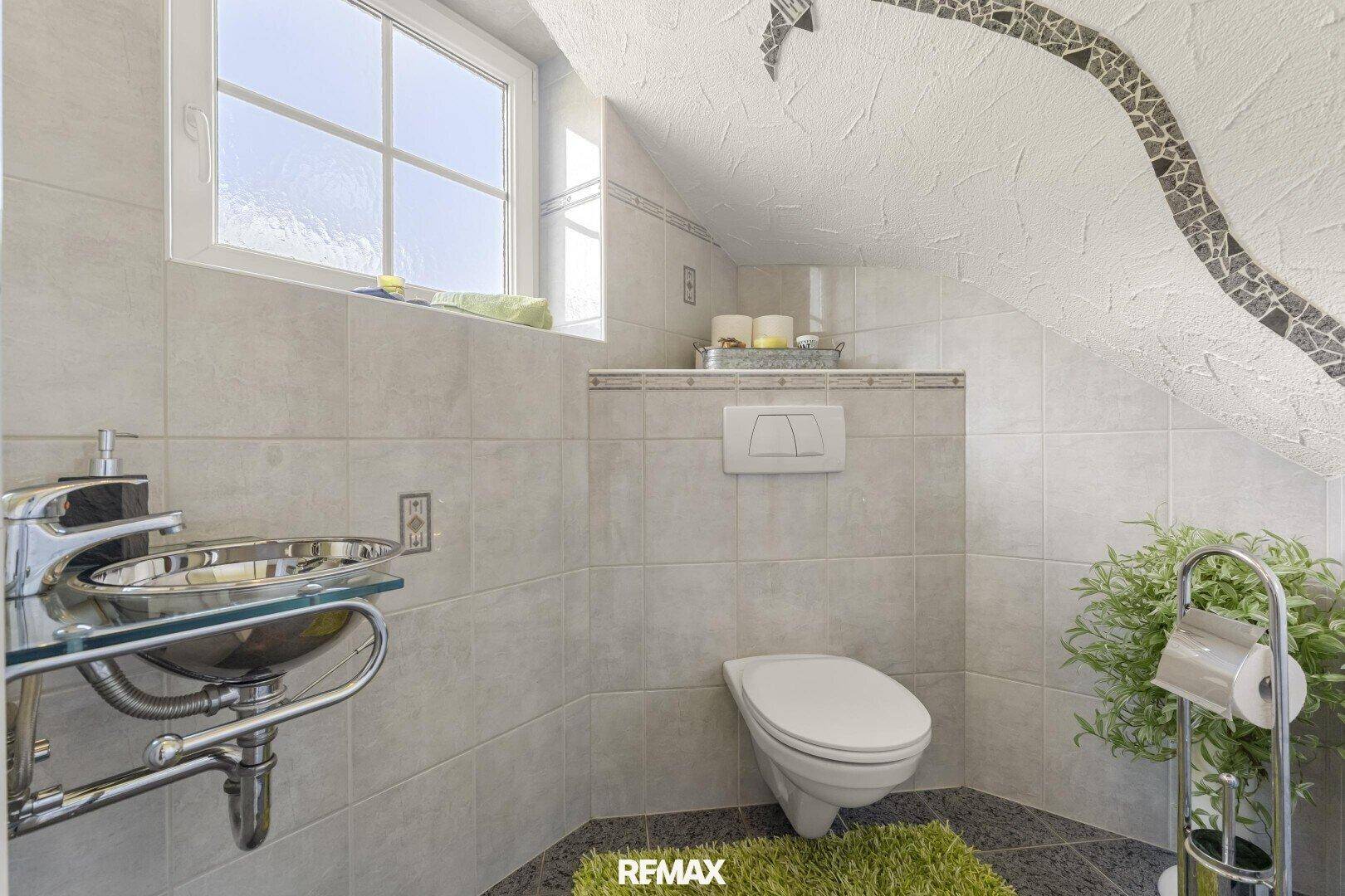 Kleines Badezimmer mit WC, modernem Waschbecken und Fenster unter einer Dachschräge.