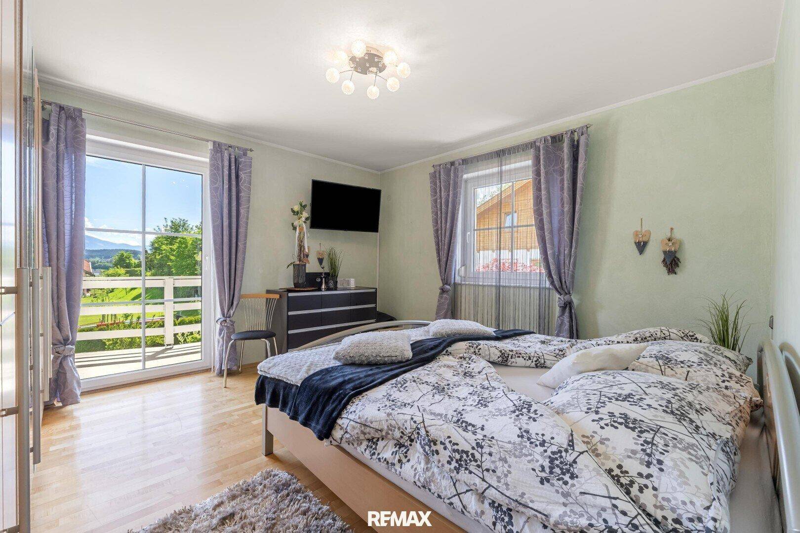 Helles Schlafzimmer mit Holzboden, großem Fenster und Balkonzugang mit Bergblick.