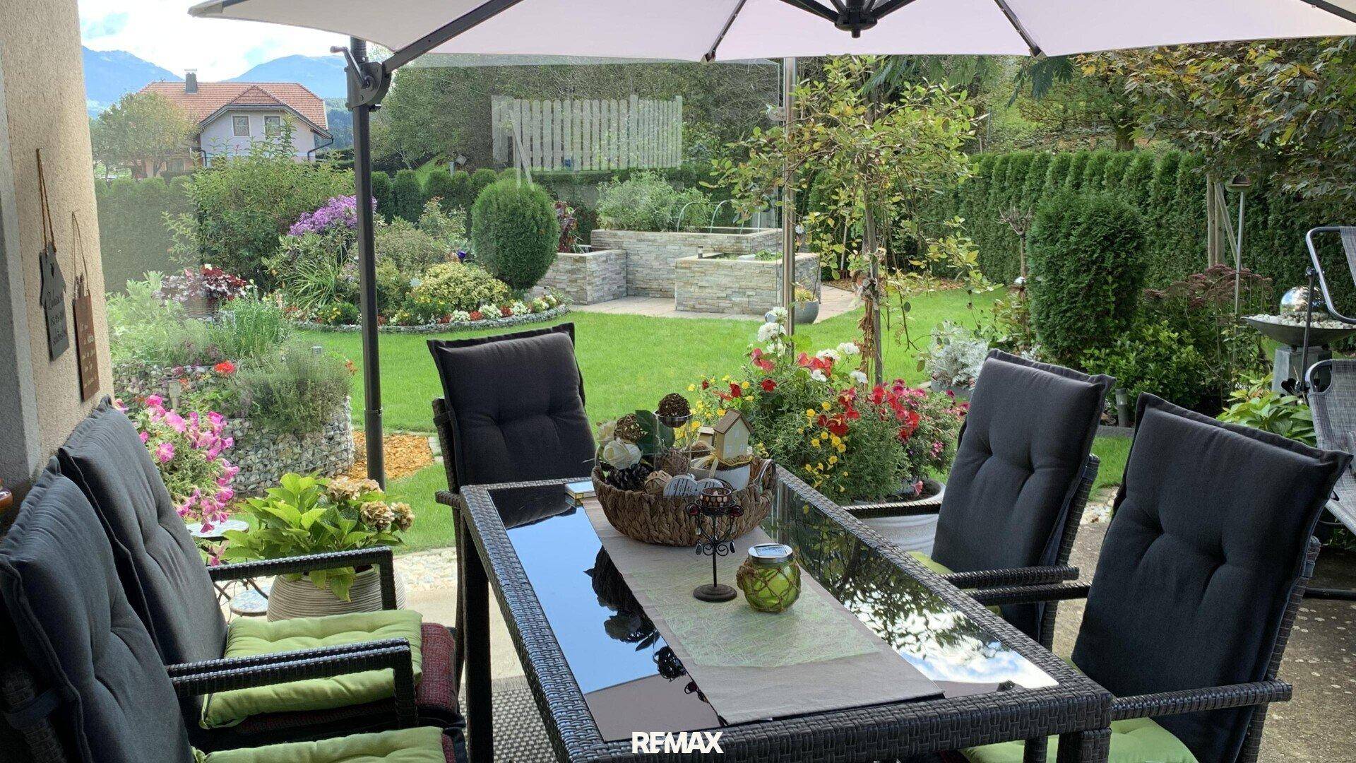 Gemütliche Terrasse mit Esstisch und Stühlen, umgeben von einem blühenden Garten und viel Grün.