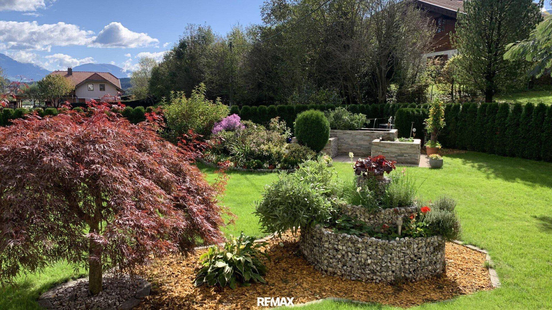 Farbenfroher und liebevoll gestalteter Garten mit verschiedenen Pflanzen, Blumenbeeten und Steindekorationen.