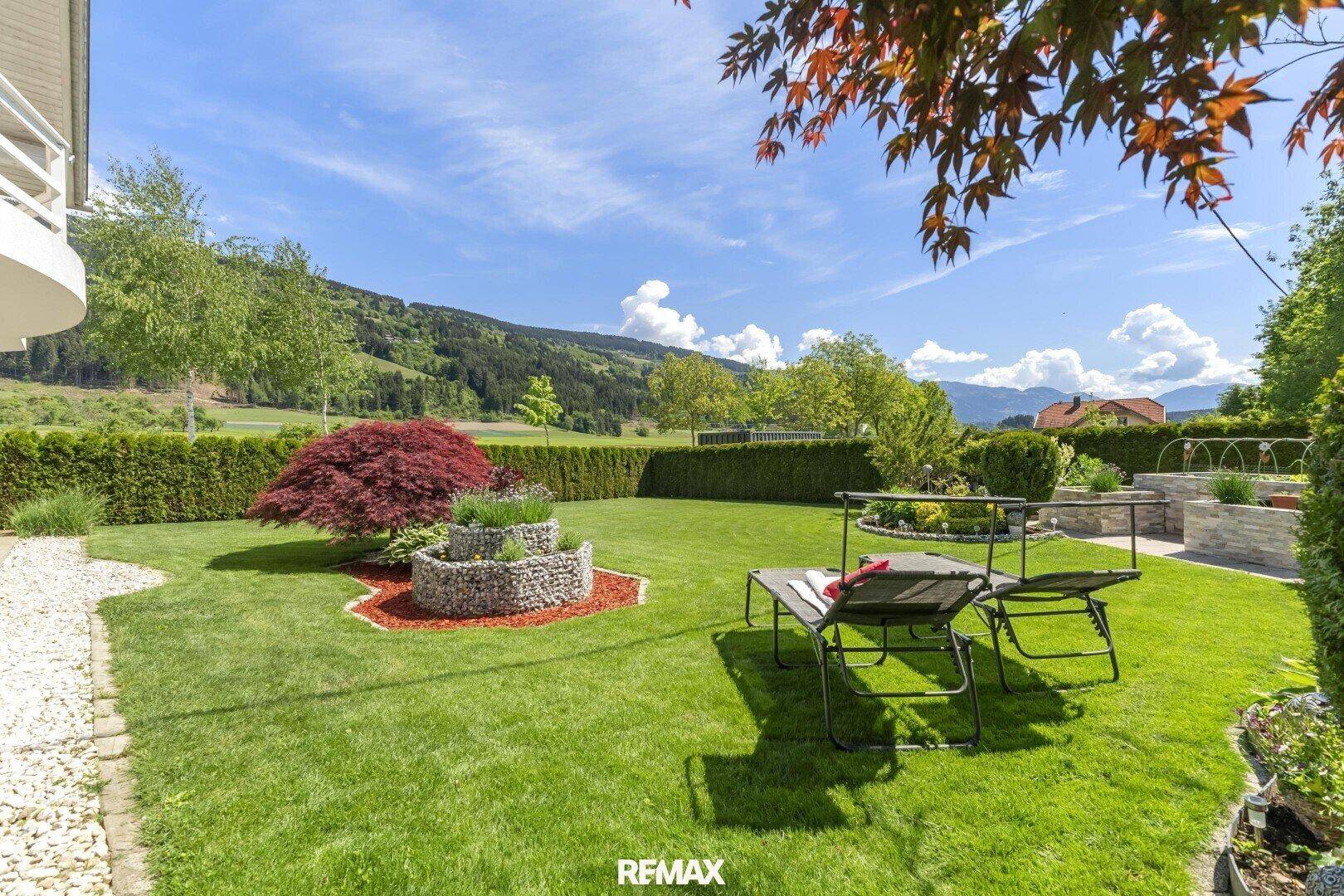 Sonniger Garten mit Liegestühlen, dekorativen Steinelementen und weitem Blick auf die Landschaft.