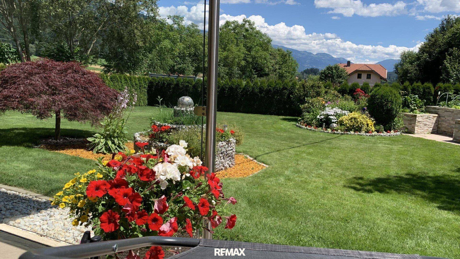 Blick vom Terrassenbereich in den weitläufigen, gepflegten Garten mit bunten Blumen und Rasenflächen.